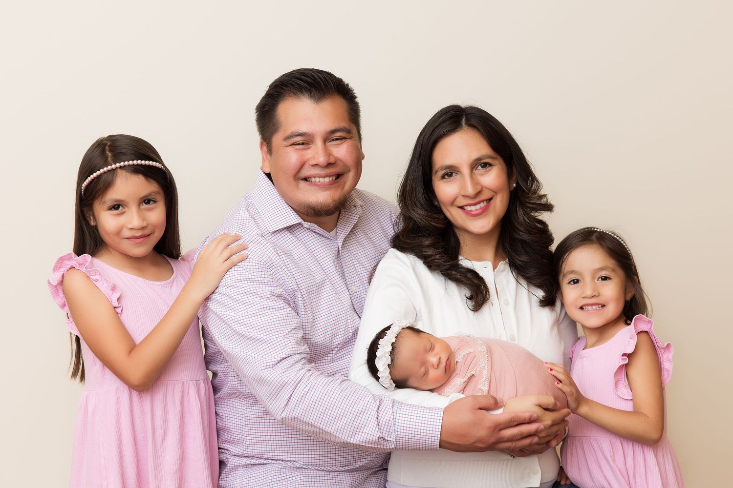 Happy family portrait with parents and daughters in coordinated pink and white outfits.