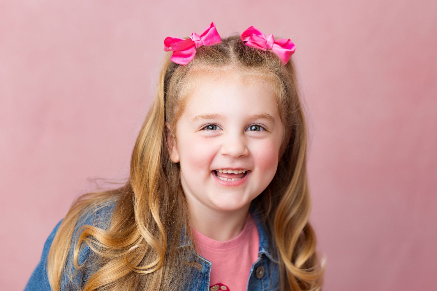 Portrait series of young child with pink hair bows against rose colored background.