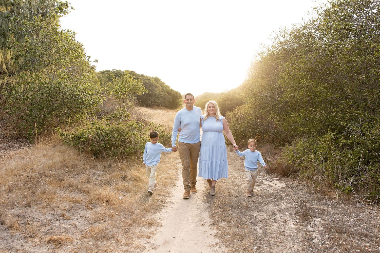 Family walking together on nature trail at sunset wearing coordinated blue outfits.