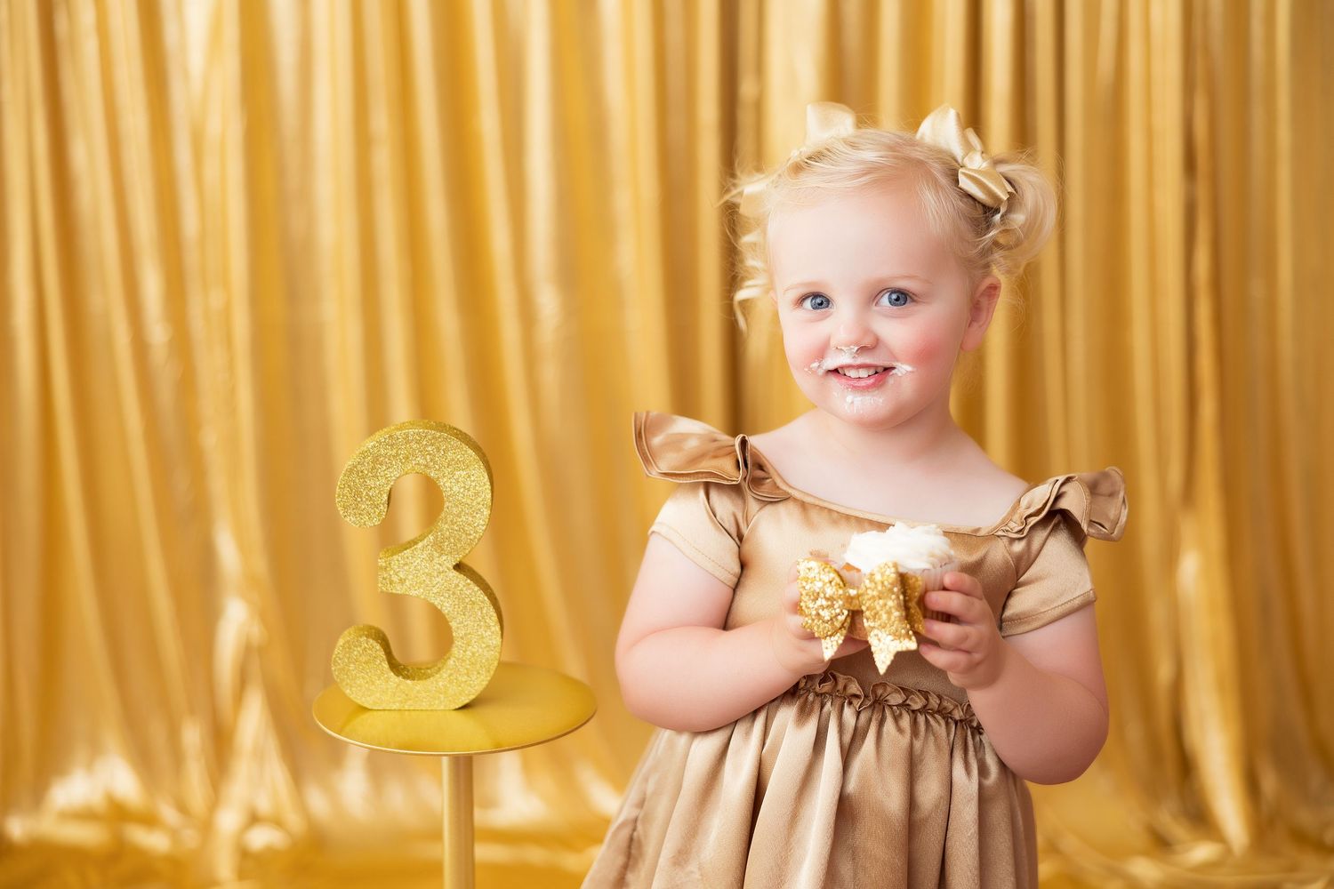 Golden themed first birthday party decorations with metallic balloons and curtains create a luxurious celebration setting.