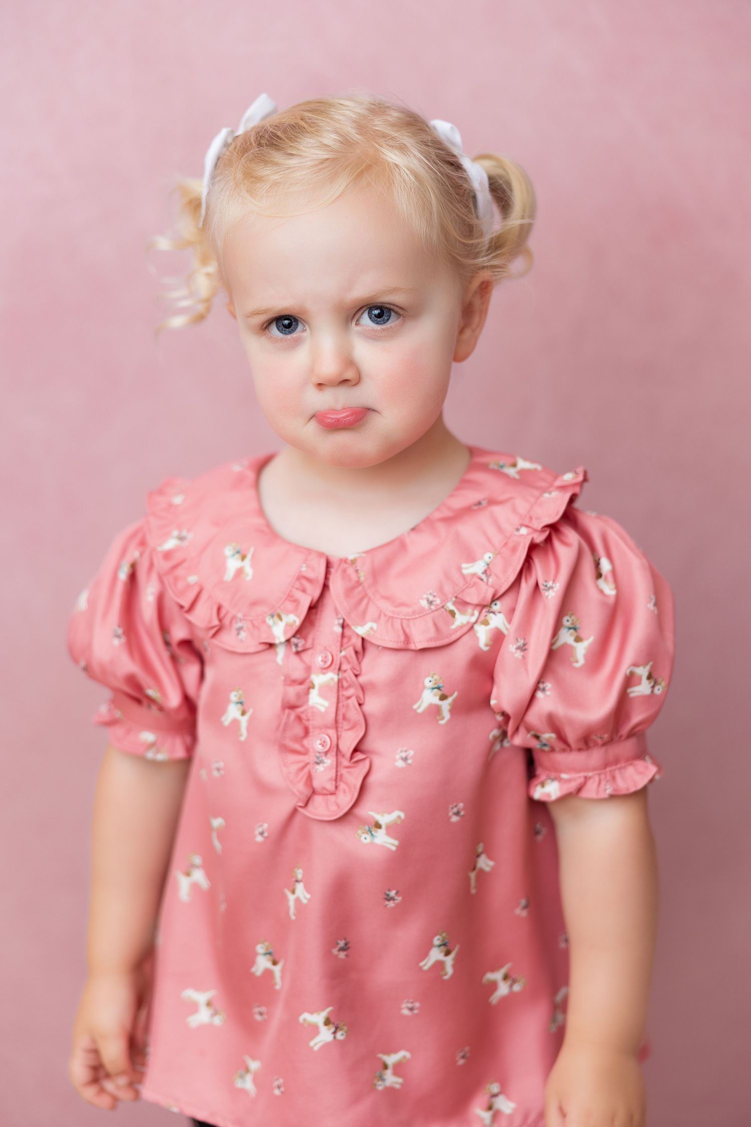 Sweet portrait of a young child in a pink floral dress with puffy sleeves against a rose-colored background.