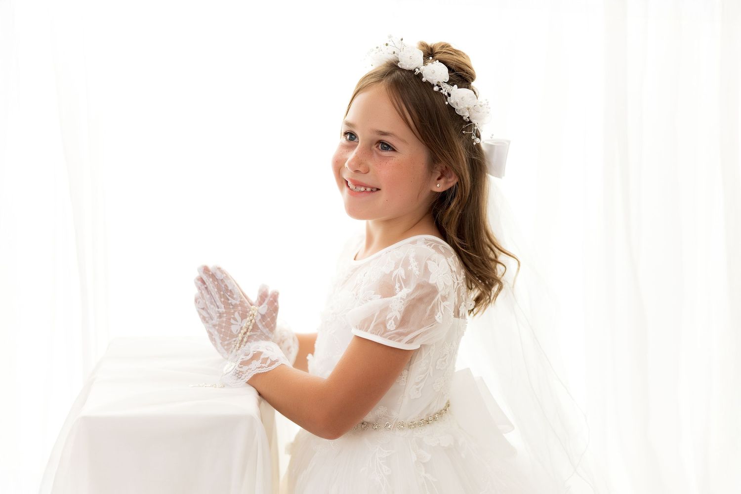 A smiling bride in a white wedding dress kneeling and holding a pillow.