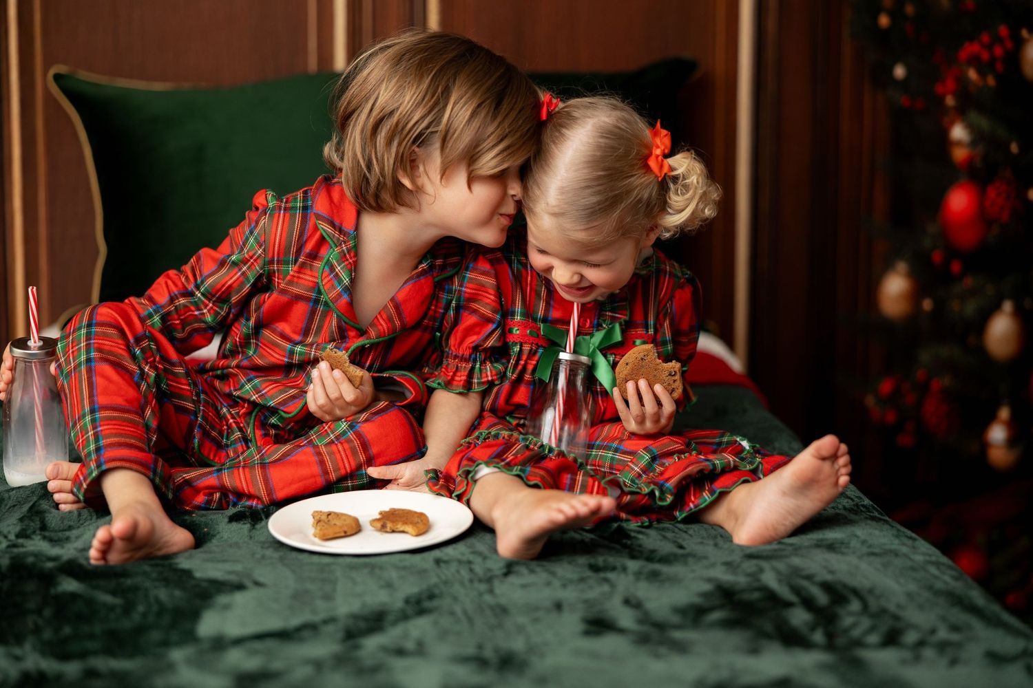 Siblings in matching red plaid Christmas pajamas sharing milk and cookies by the tree at a Pacific Grove holiday mini session