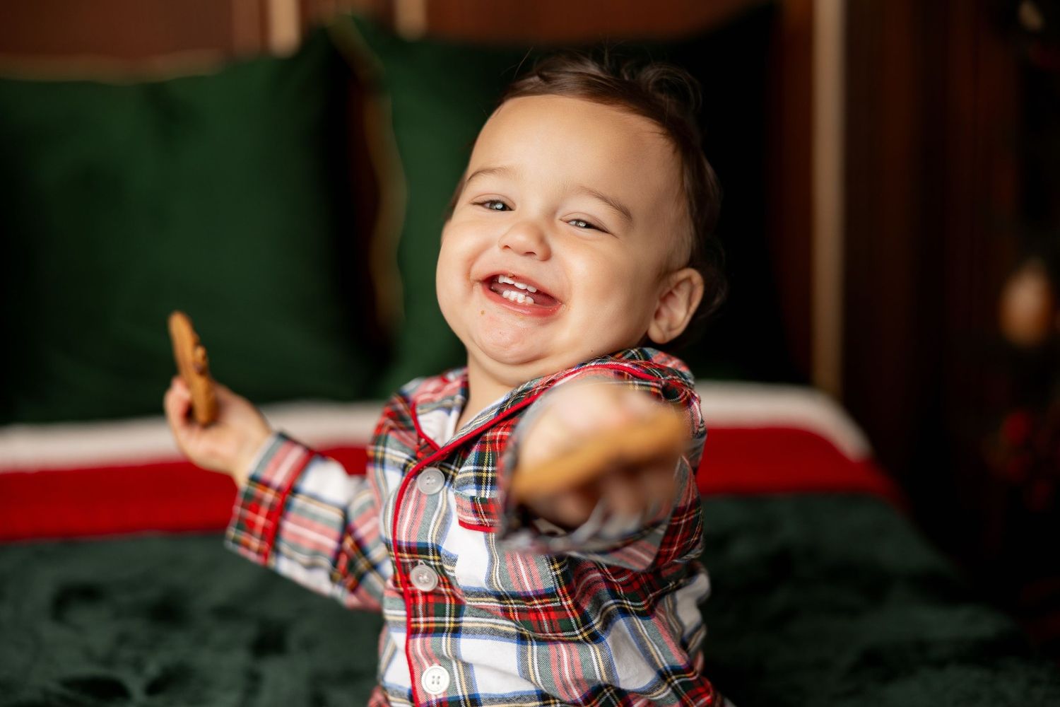 Smiling toddler in plaid Christmas jammies holding cookies at a Milk & Cookies holiday mini session in Pacific Grove