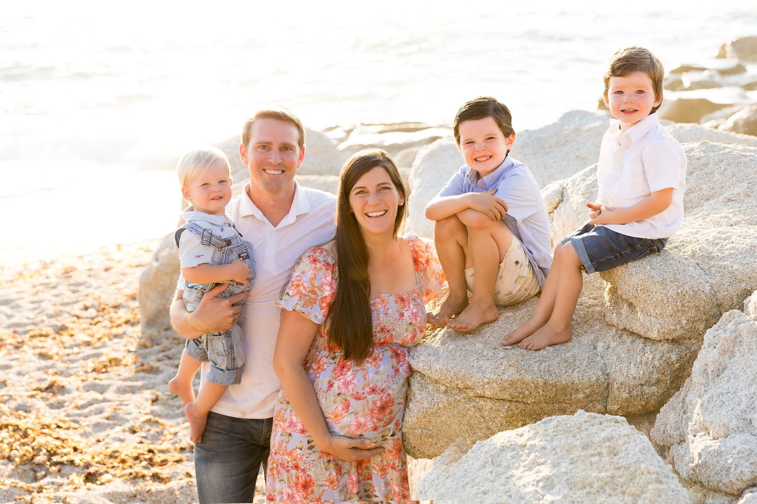 Family sitting together on coastal rocks during golden hour photoshoot.