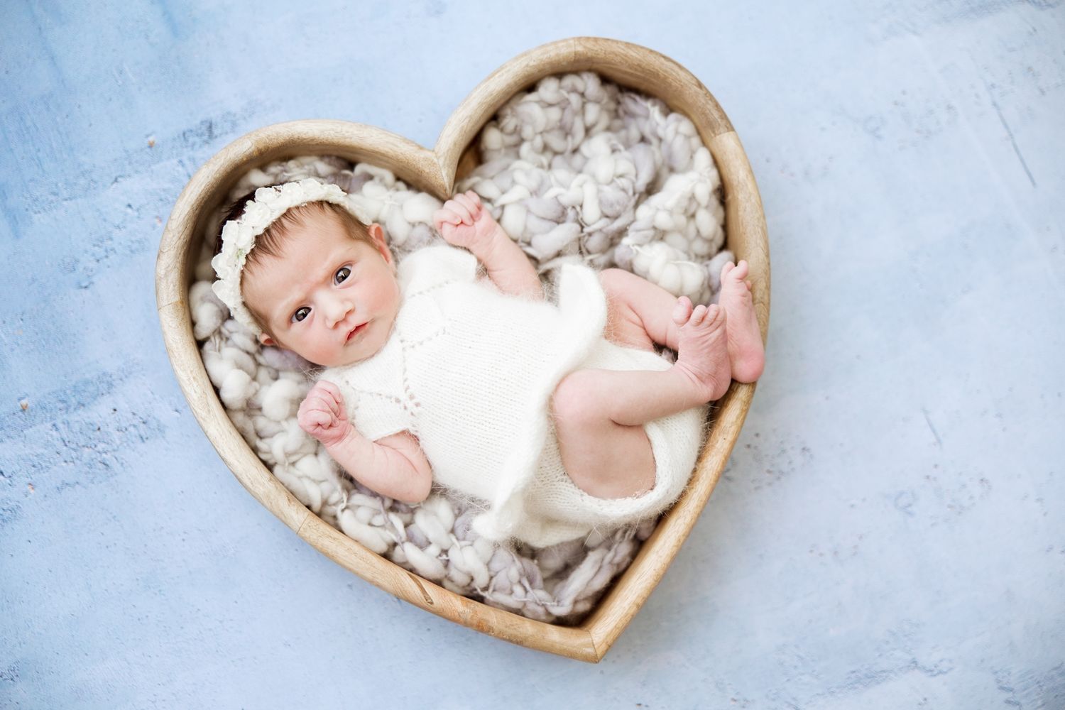 A collection of heart-shaped wooden bowls with soft cotton filling and sleeping newborns arranged in a row.