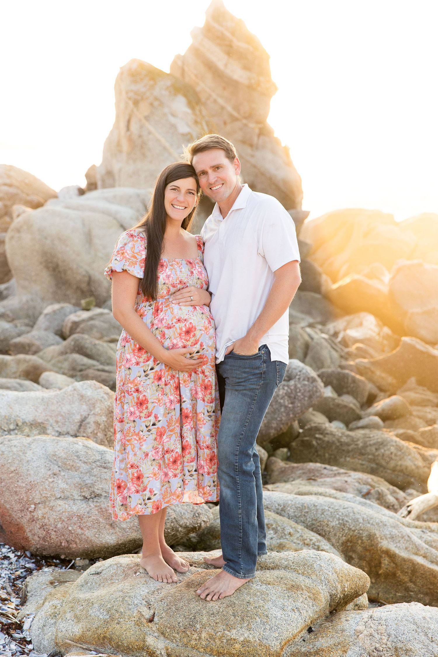 Couple embraces on rocky shoreline during golden hour sunset photo session.
