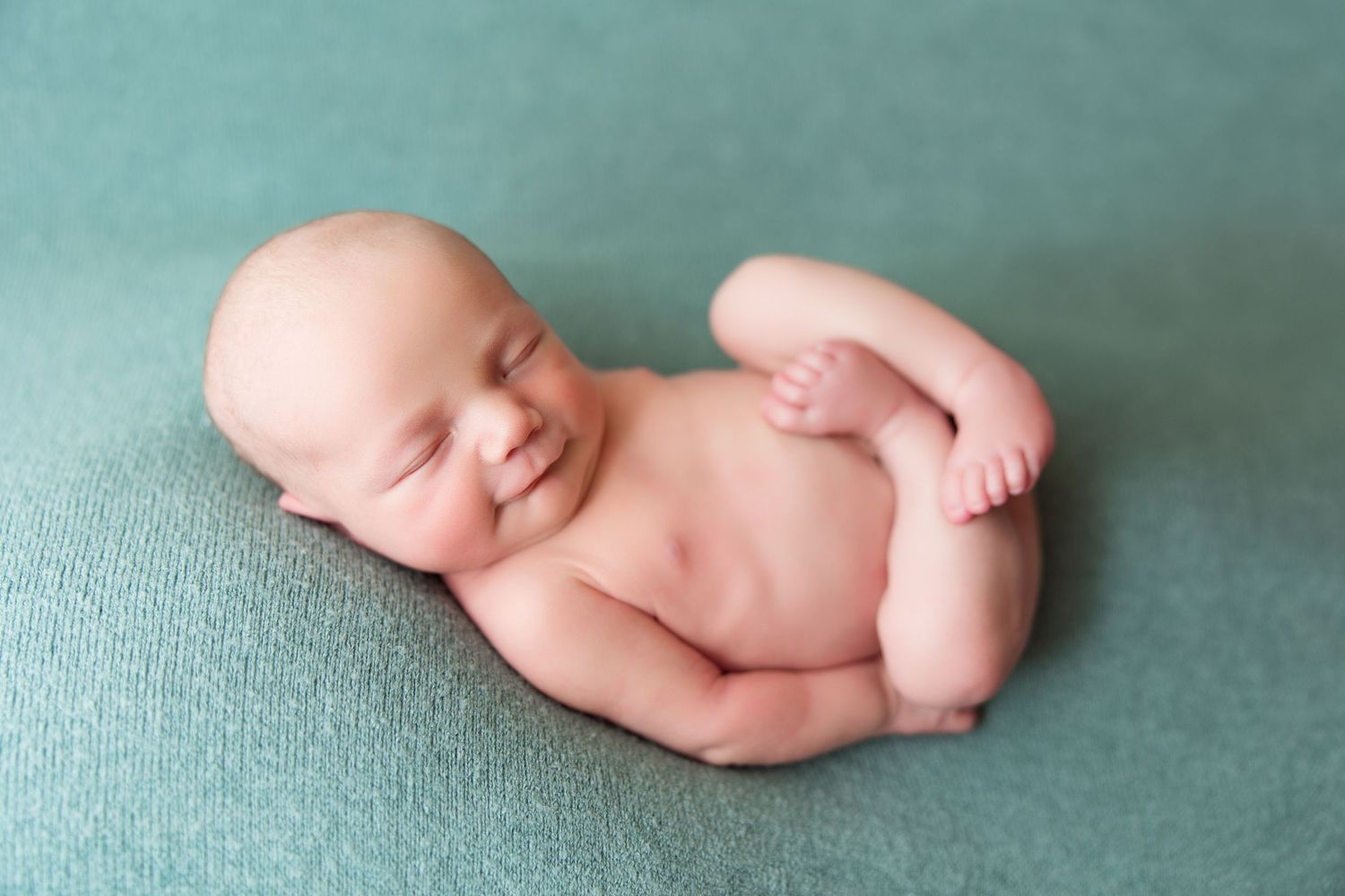 Peaceful newborn resting on teal background in natural pose.