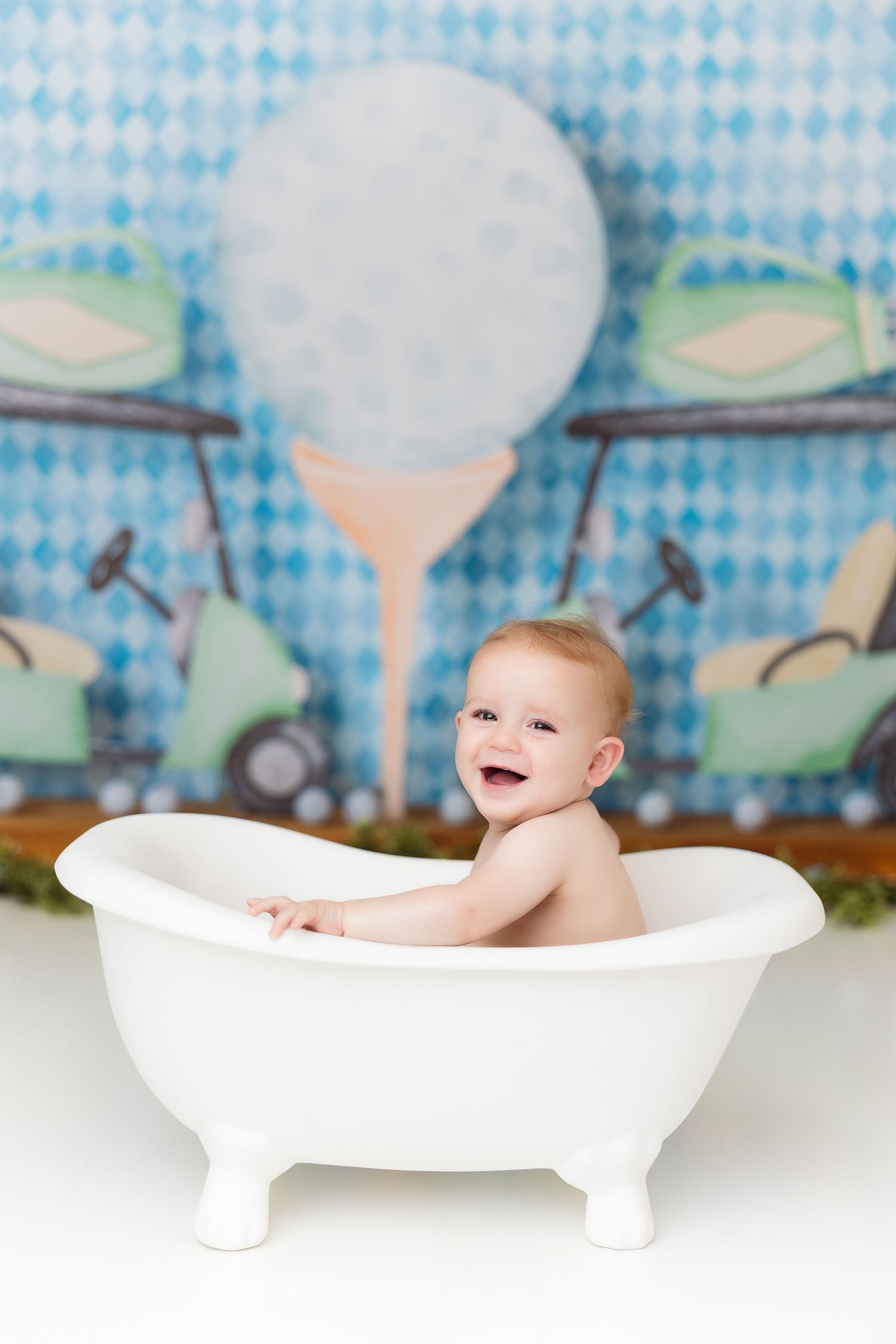Baby sitting in vintage white clawfoot bathtub against whimsical blue patterned backdrop.