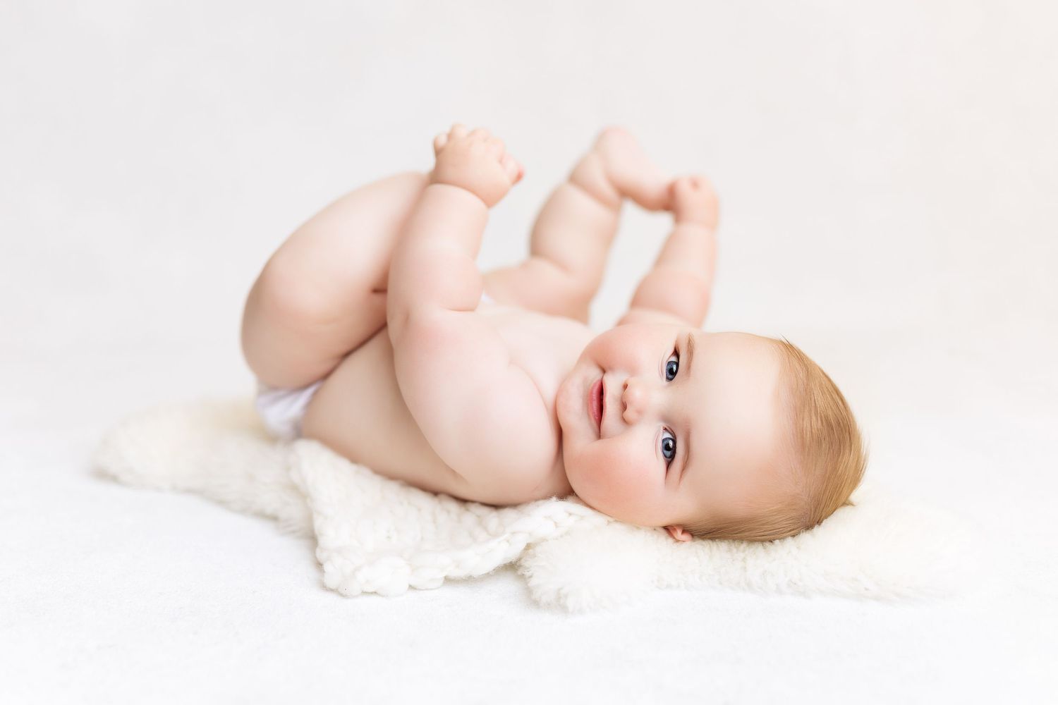 Playful baby lying on back on white fuzzy blanket.