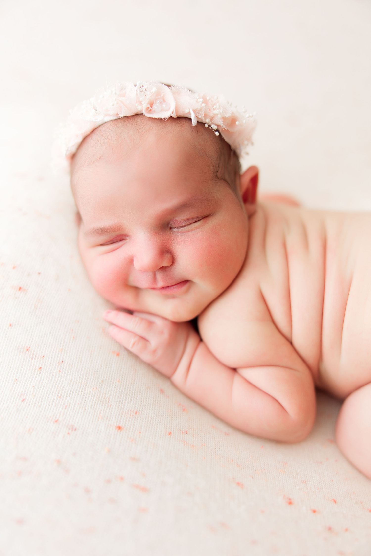 Peaceful sleeping baby with pink headband resting on soft white fabric.