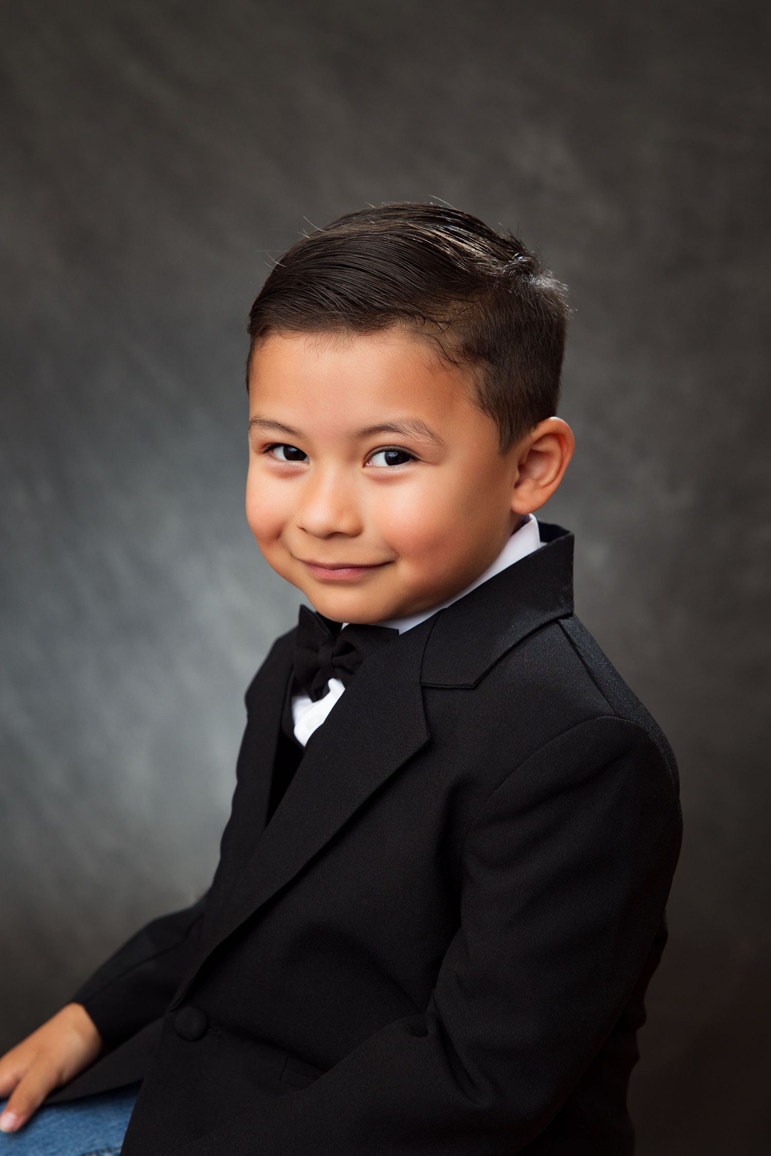 Professional studio portrait of child in black suit against gray background with various poses showing playful expression.