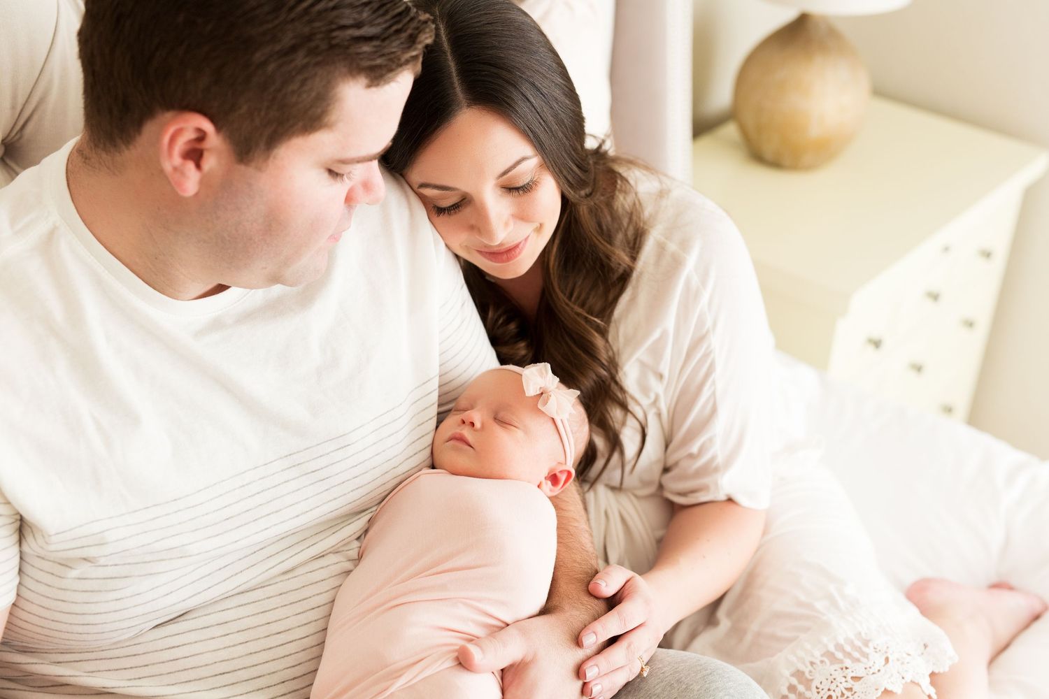 Tender newborn photography session with parents snuggling on plush bed with cream bedding.