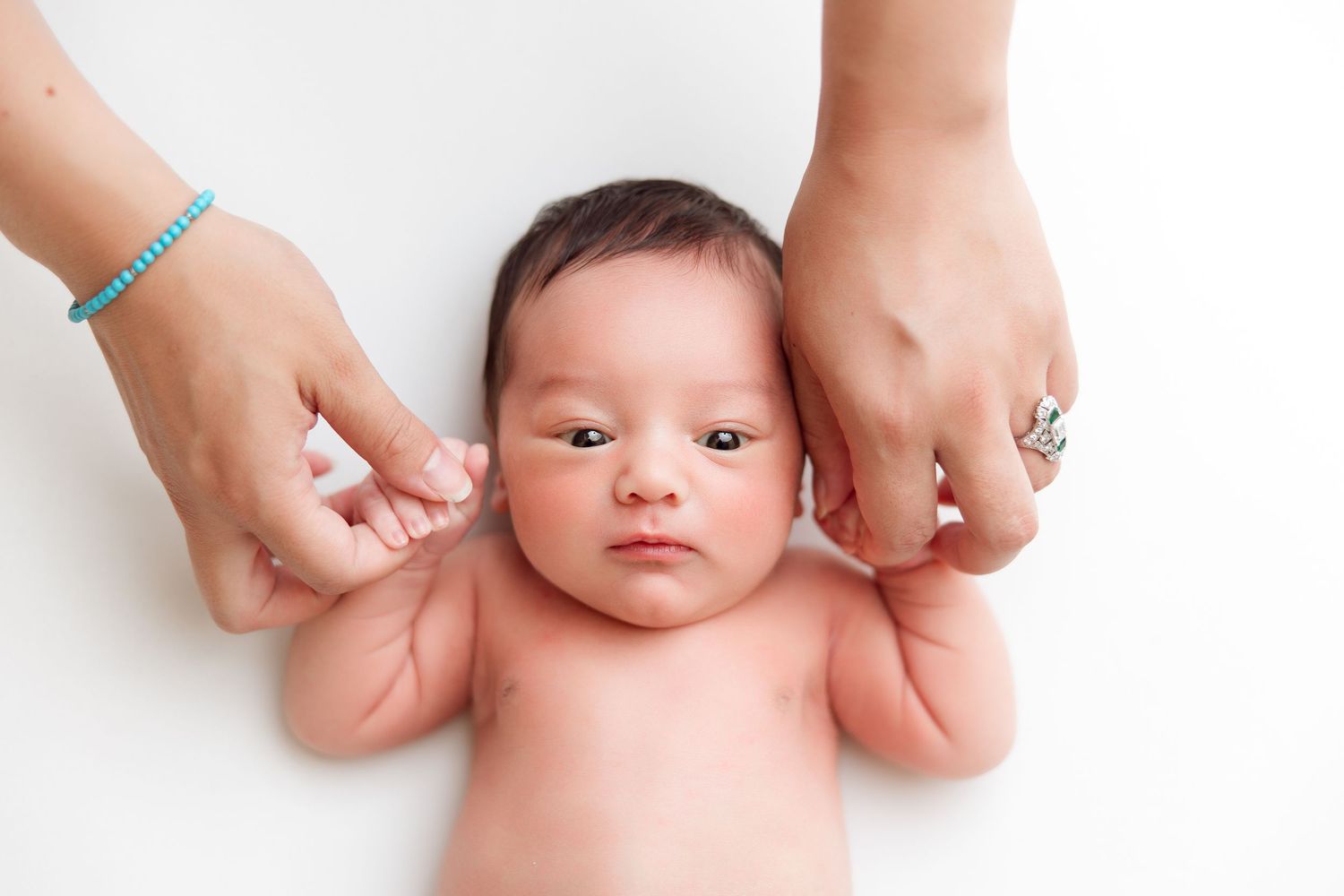 Adult hands gently supporting small baby on white background.