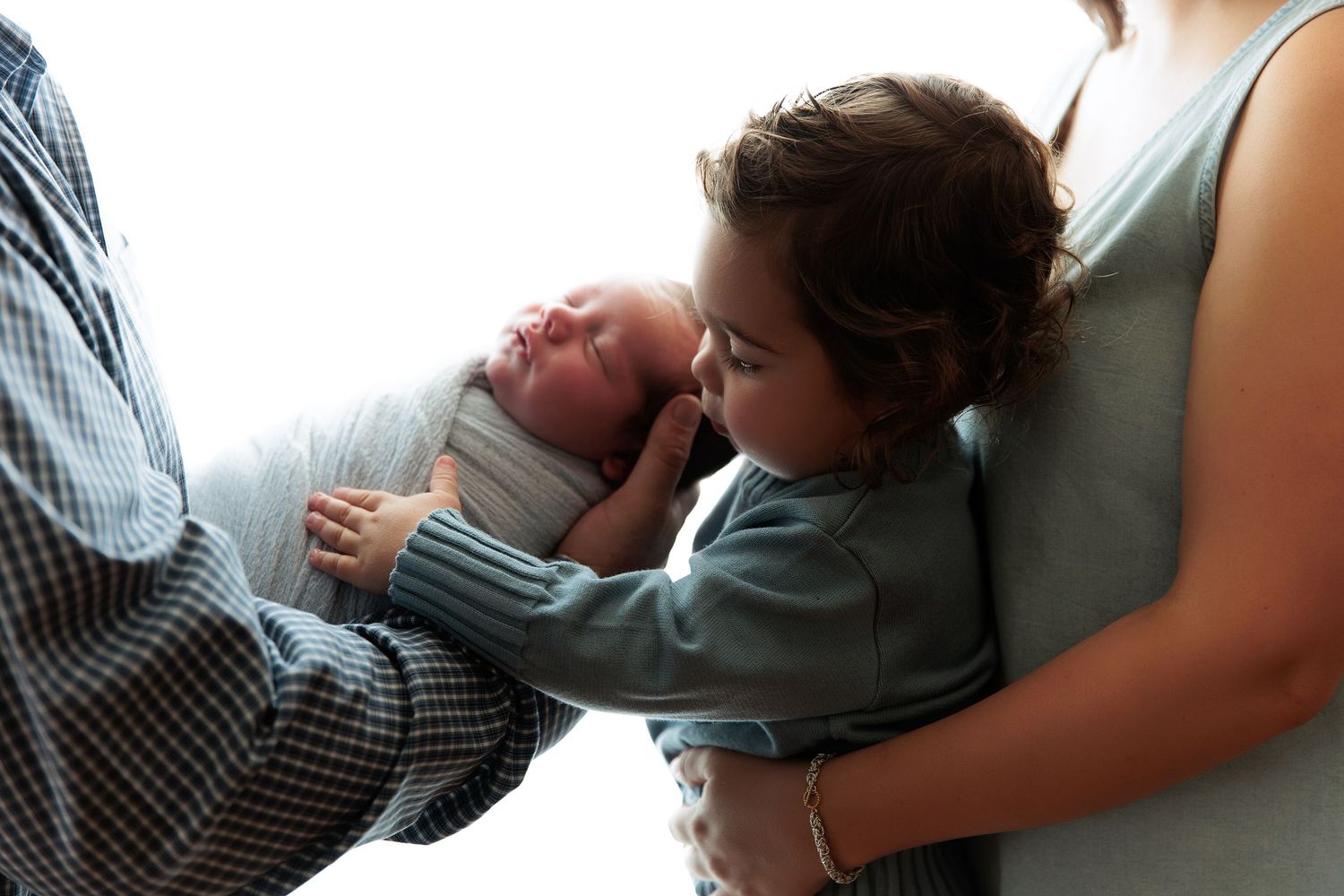 Parent cradling newborn in tender embrace against neutral backdrop.