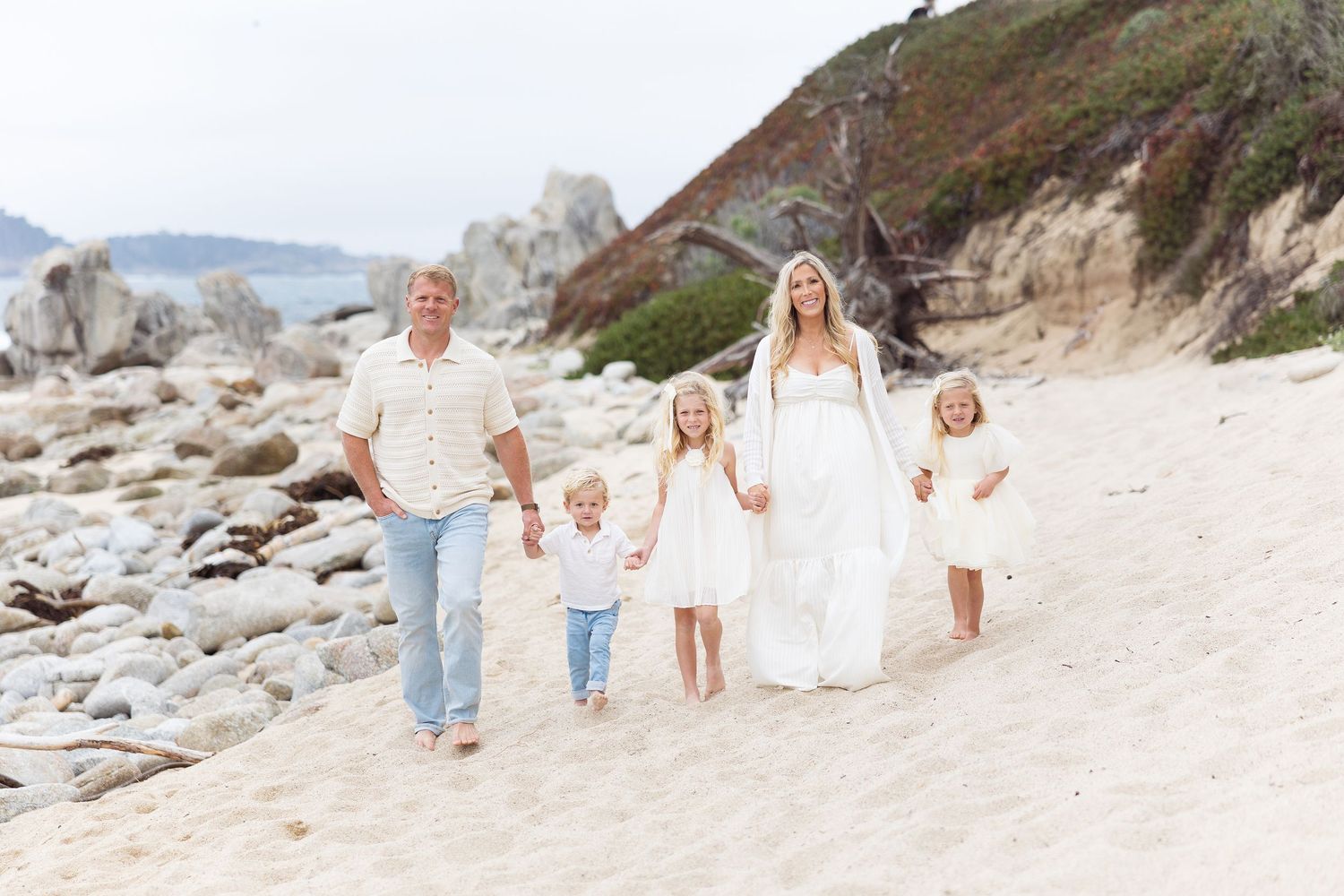 Group walking along sandy beach with ocean cliffs in background during sunset.