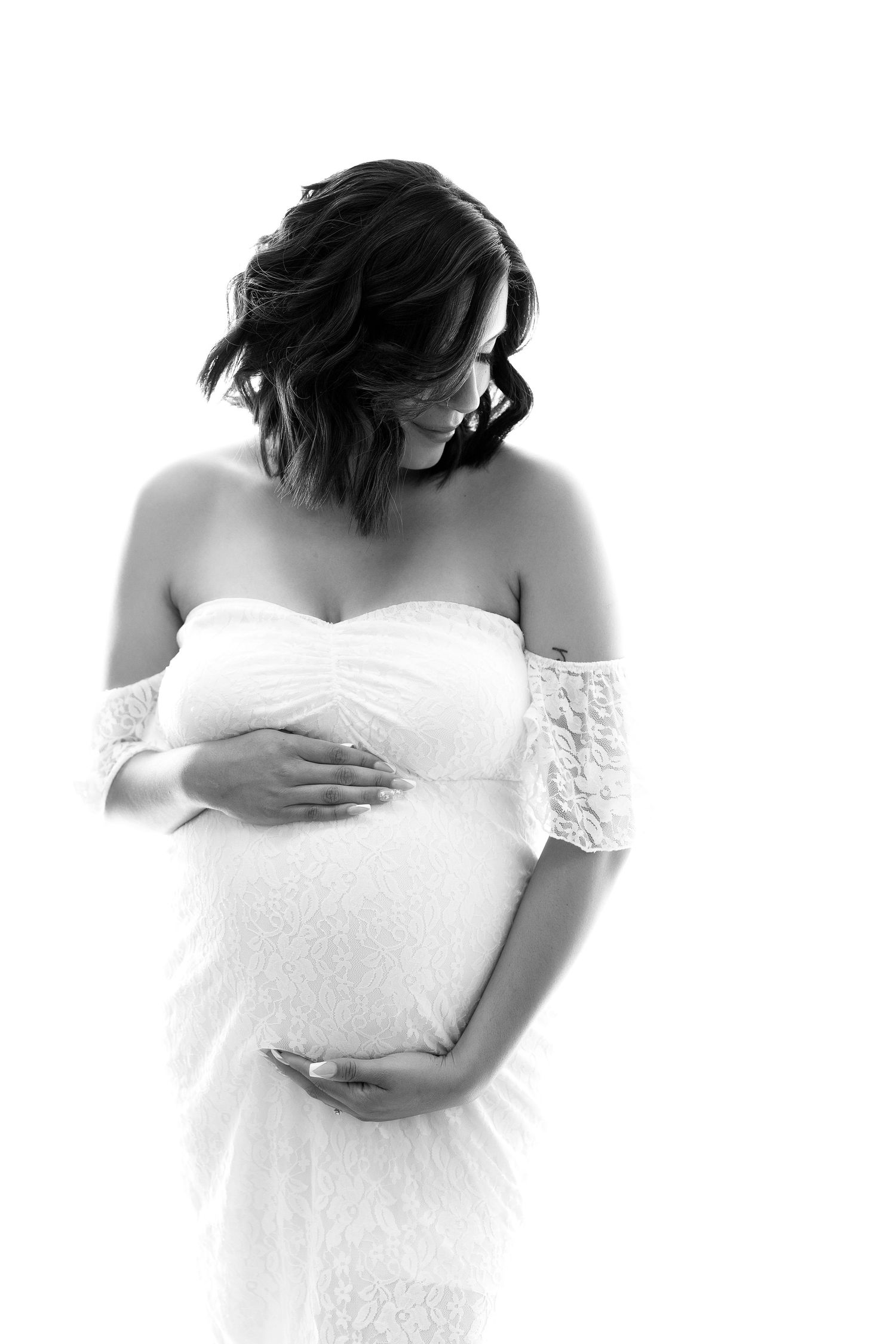 Artistic black and white maternity portraits showing pregnant figure in off-shoulder lace dress.