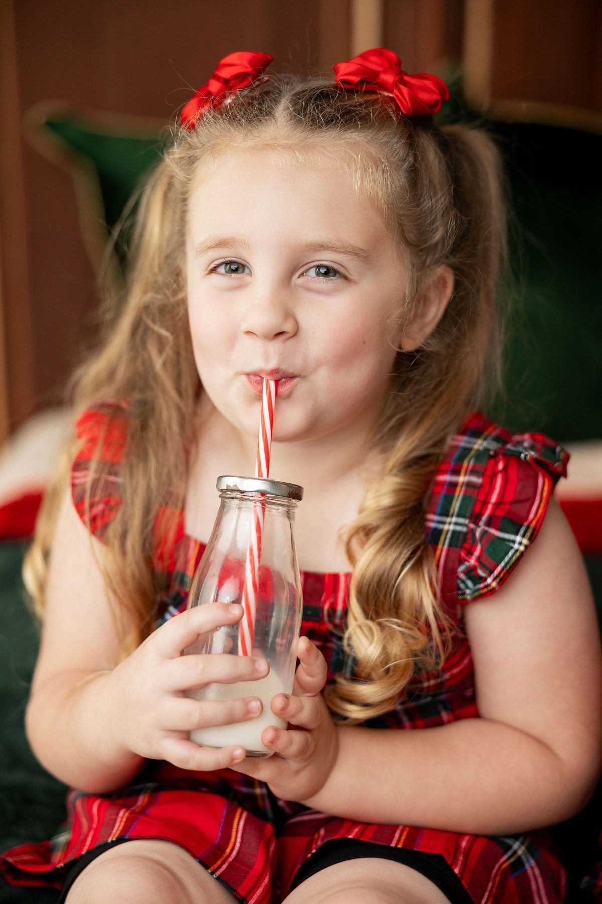 Toddler in a plaid Christmas dress sipping milk from a bottle with a striped straw, Pacific Grove mini session