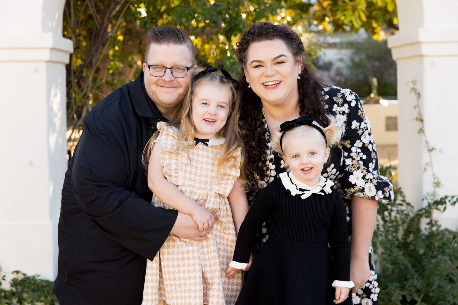 Family portrait outdoors with white columns and green foliage in background, in Monterey.