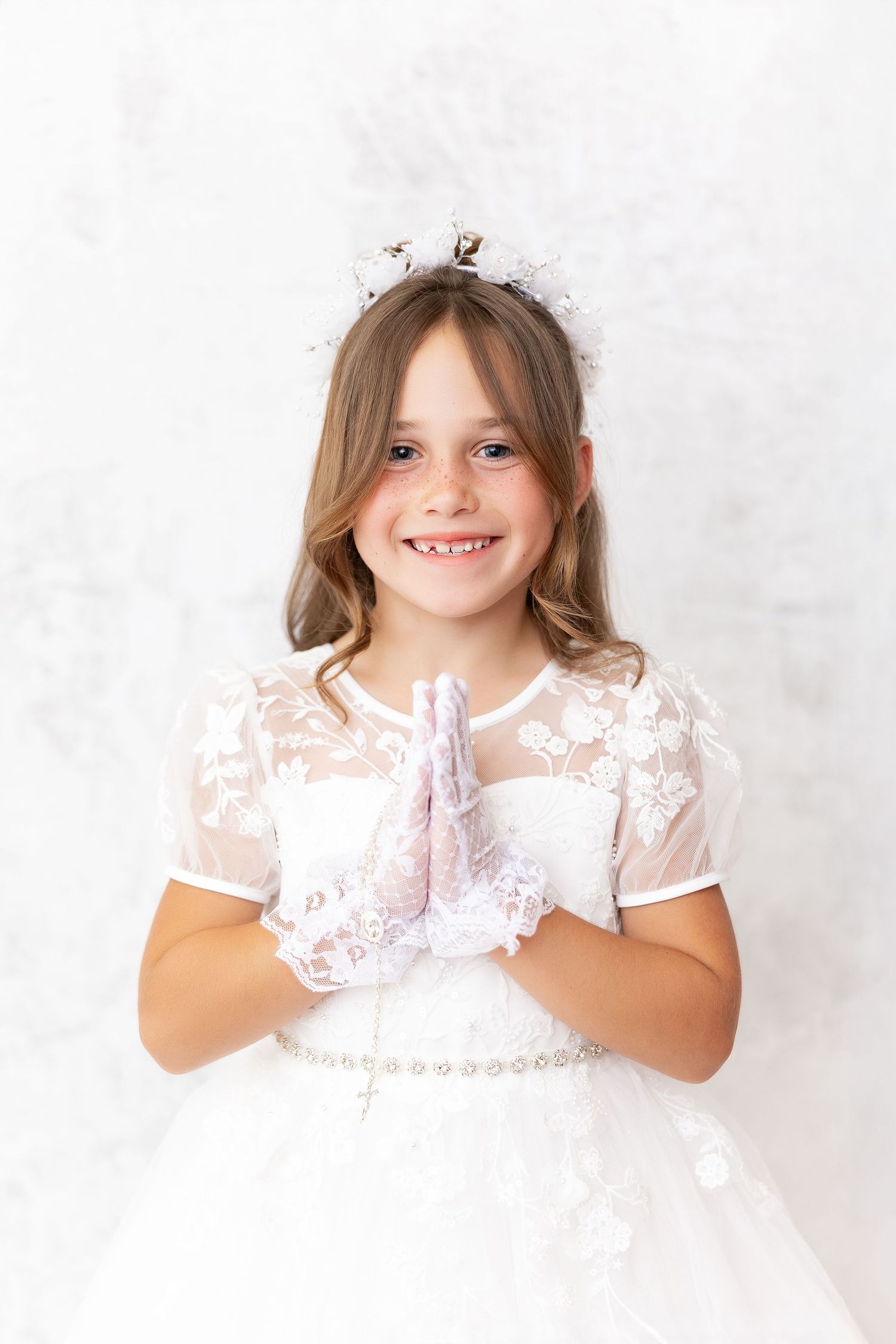 Young child in white lace dress holding their hands up in three different candid poses against light background.
