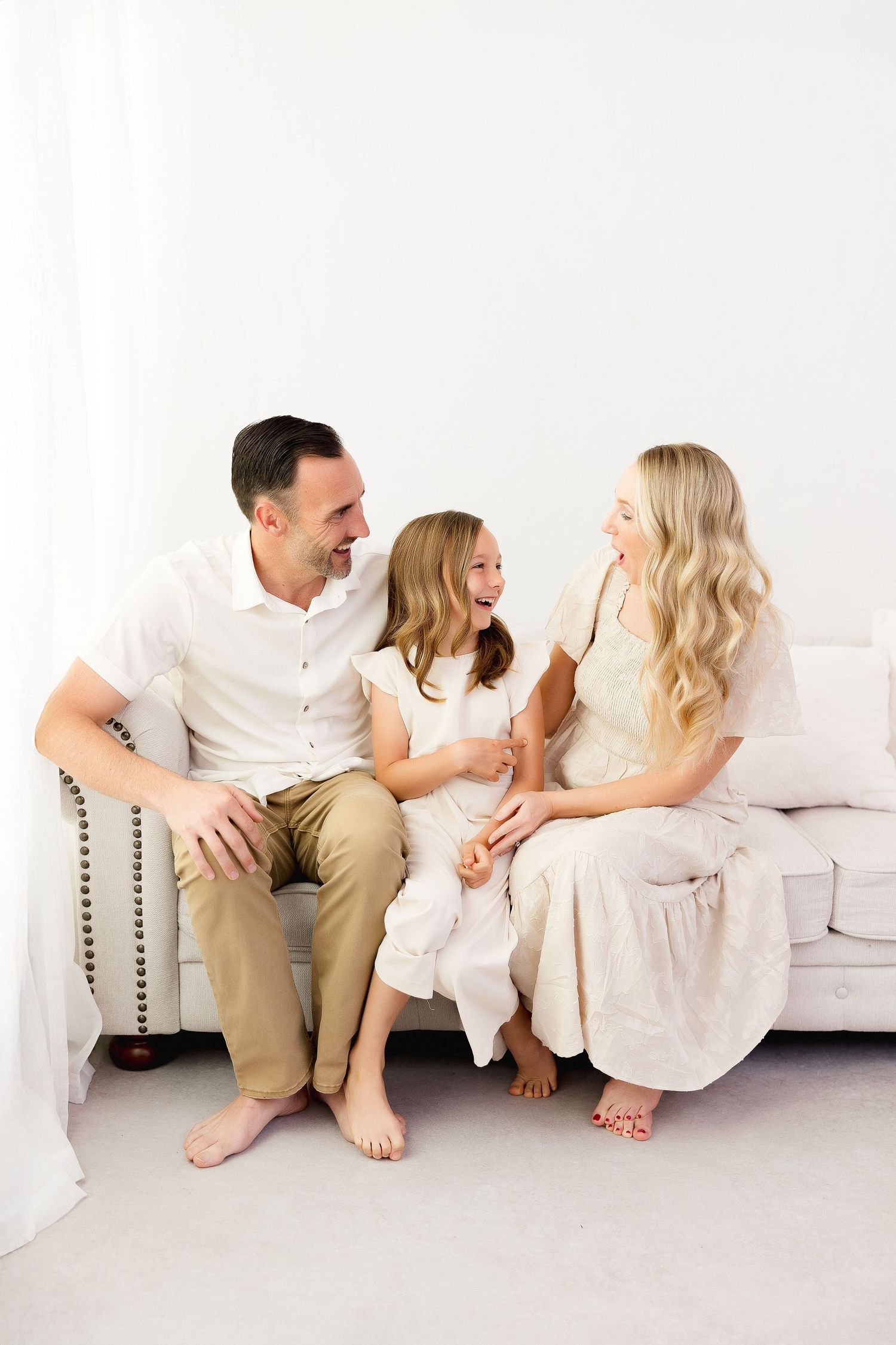 Four connected photos show a family in white clothing sitting on a couch sharing playful candid moments together.