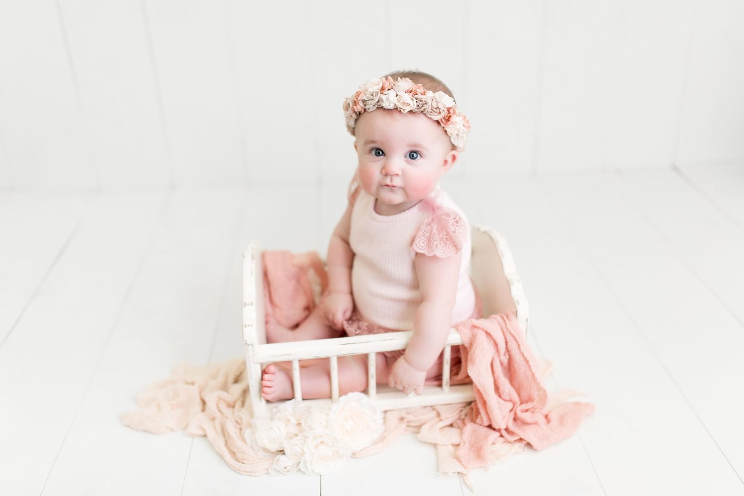 Baby photography session with soft pink tones and delicate styling on white backdrop.