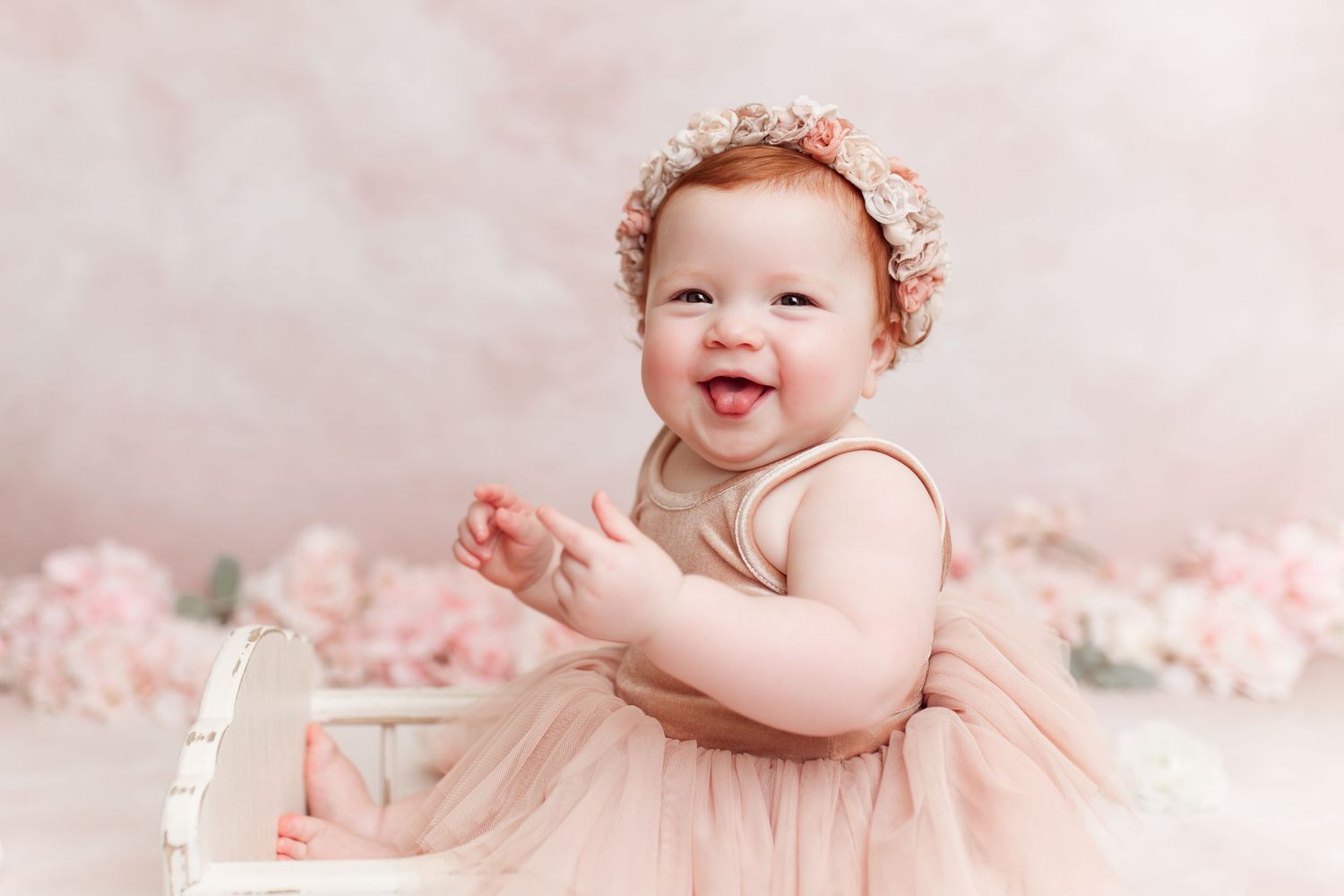 Studio portrait with soft pink tones showing a happy baby in a tulle dress with floral crown.