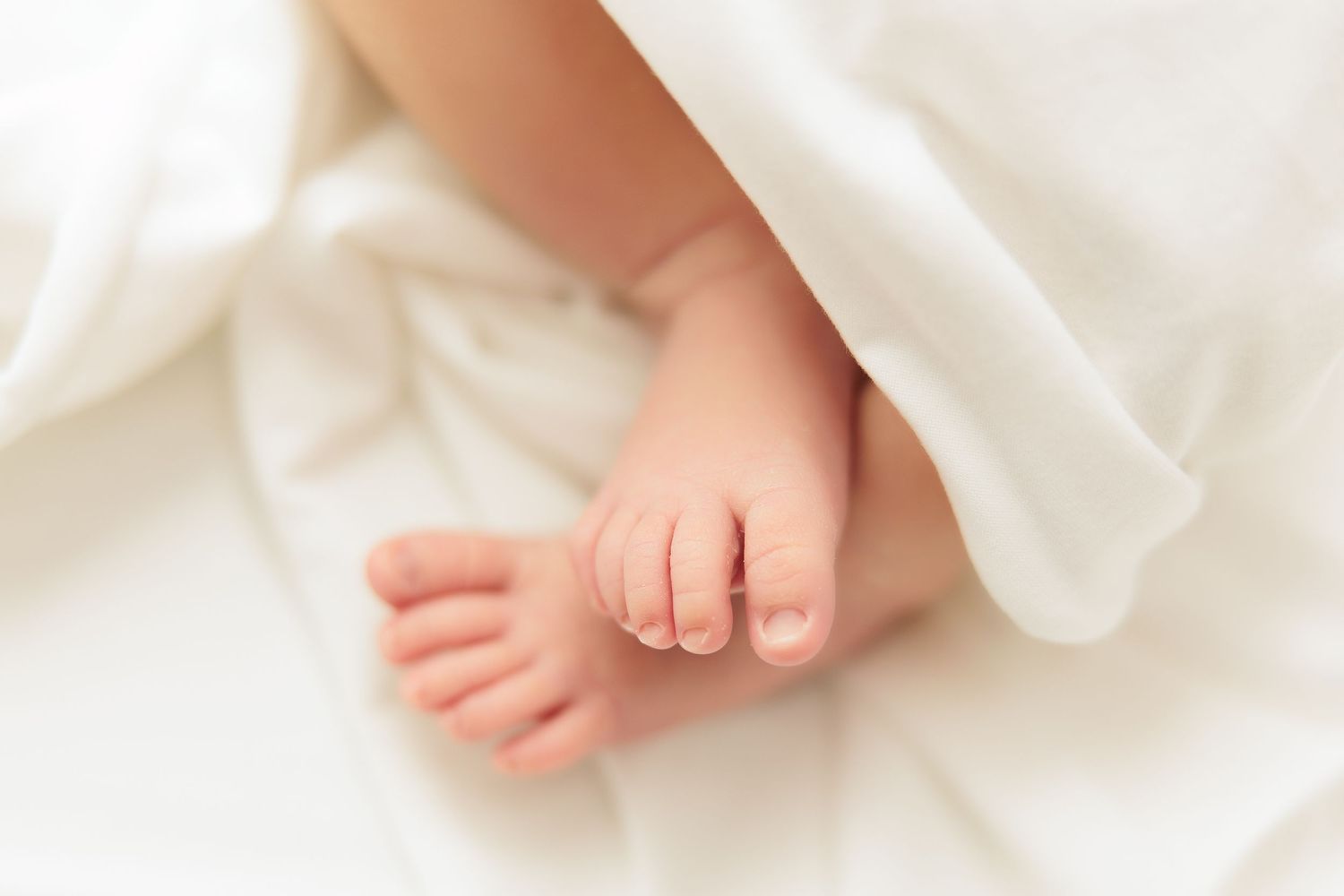 Close up of delicate newborn baby feet against white blanket.