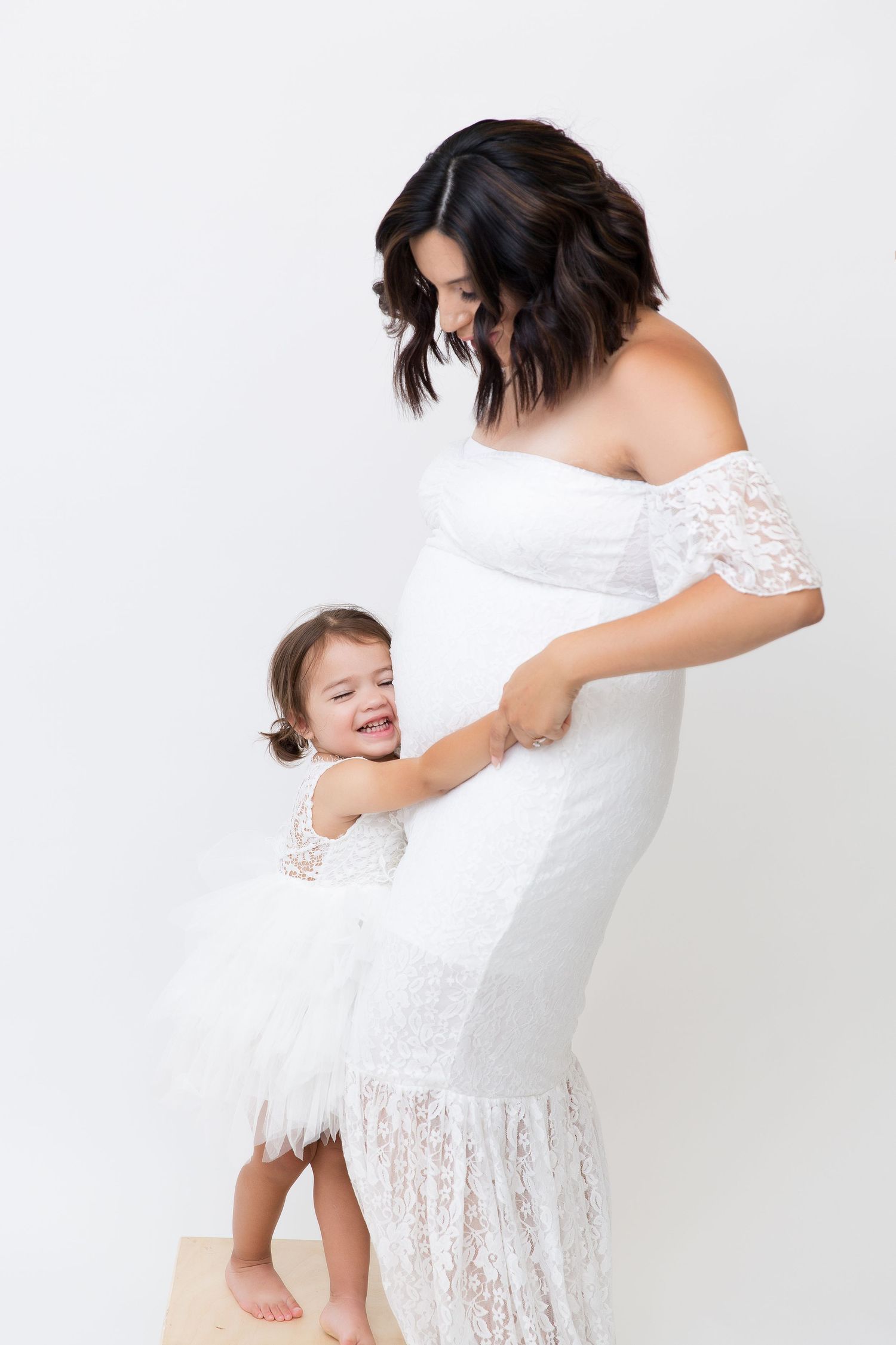 Artistic maternity photos in white lace dress against white background showing mother and child interactions.