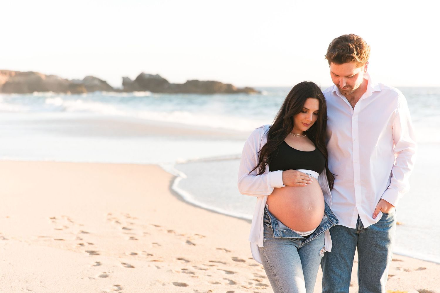 Romantic beach photoshoot with soft golden light and coastal rocks.