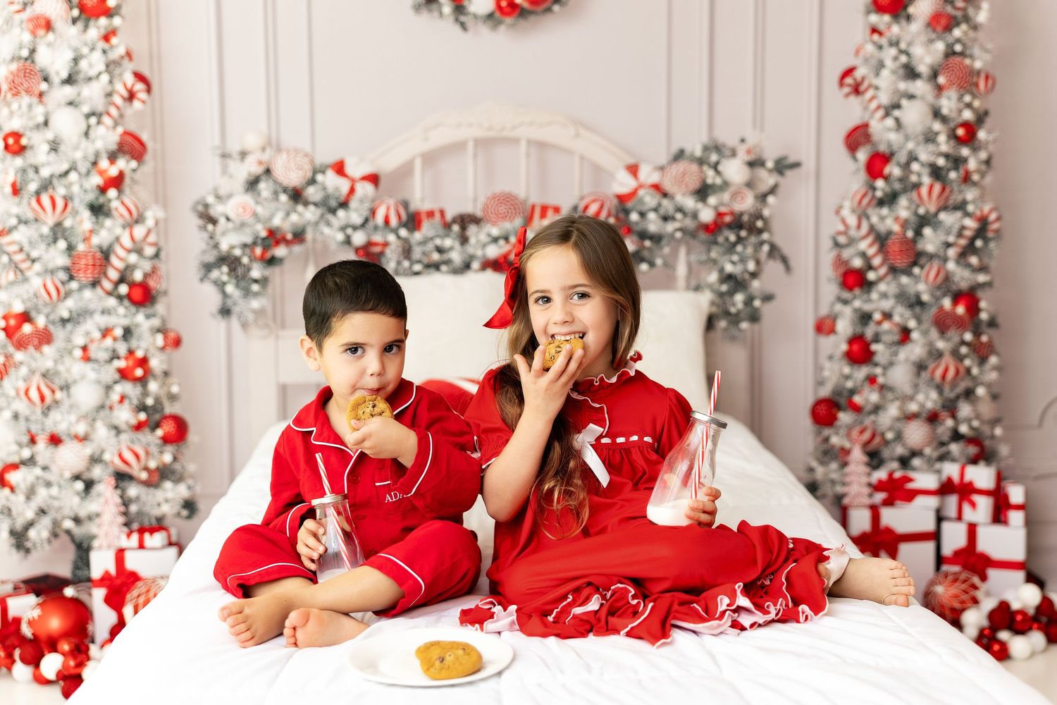 Holiday portrait session with coordinating red and white outfits against floral Christmas backdrop.