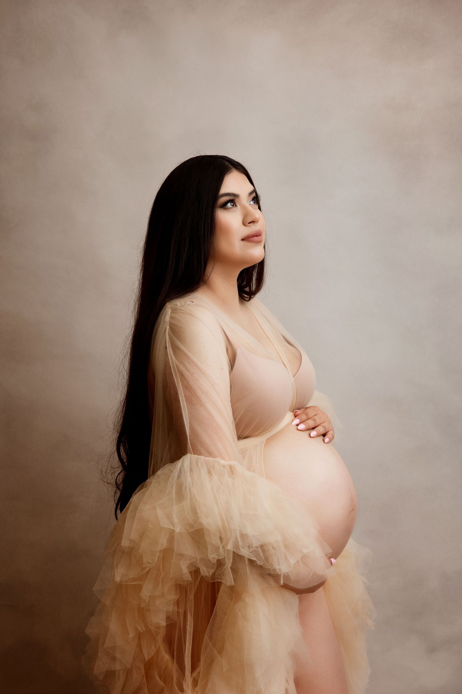 Romantic maternity portrait in sheer peach tulle gown with long dark hair.