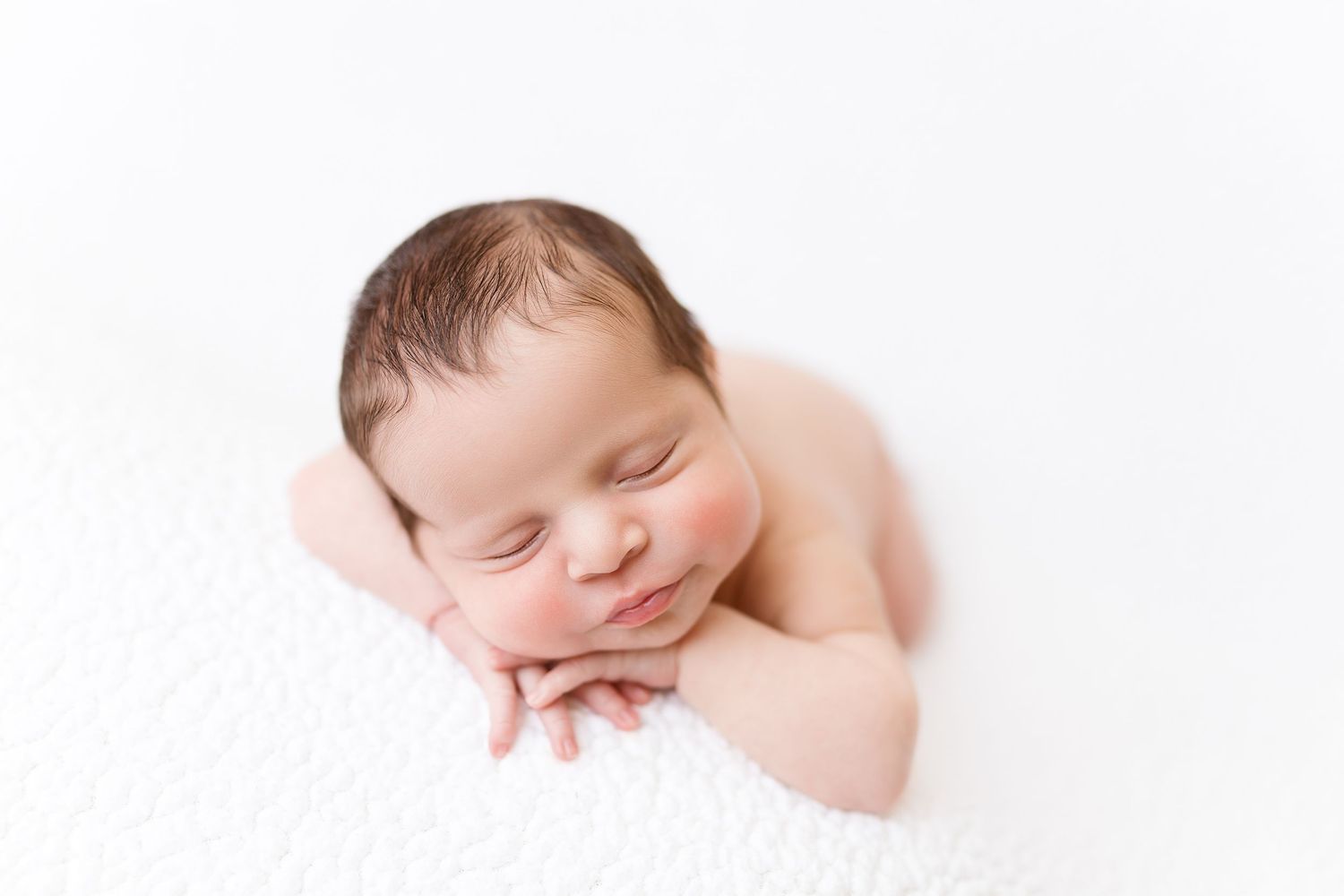 Peaceful sleeping newborn baby resting on soft white fabric in minimalist photography setup.