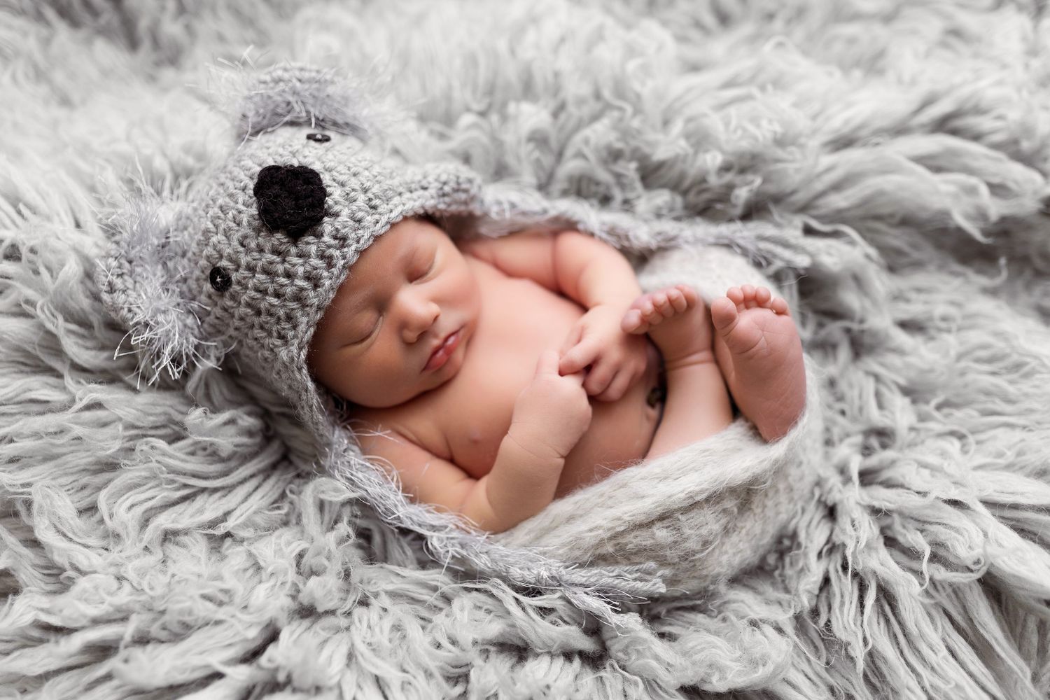 Adorable newborn baby sleeping peacefully on soft gray fur blanket in black and white photography.
