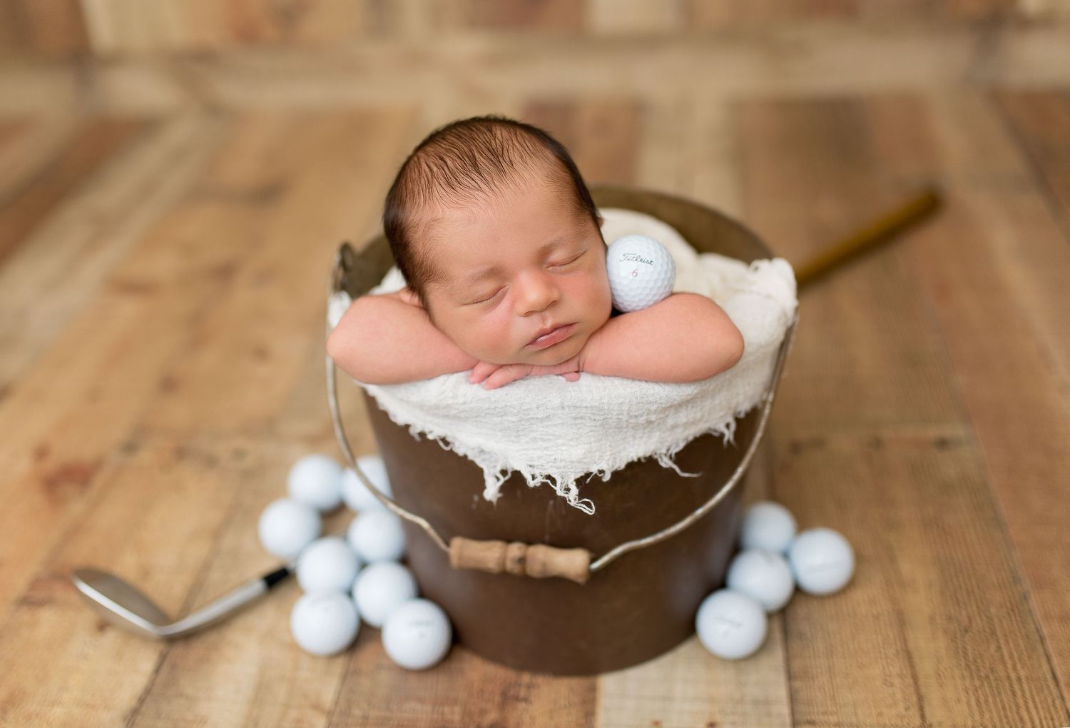 Newborn baby sleeping peacefully on wooden surface next to white decorative pom poms and string.