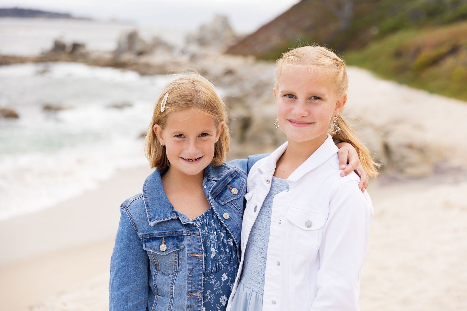 Children pose playfully on a scenic coastal beach with waves in background.