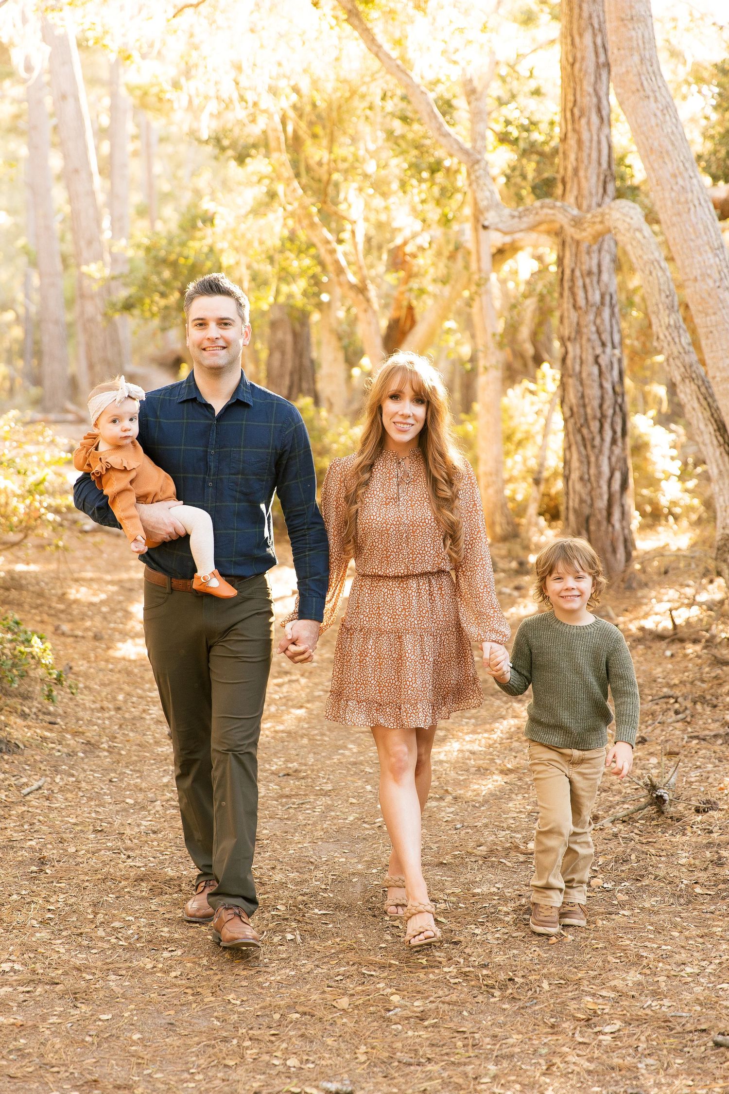 Family walking together on wooded trail in coordinating brown and orange autumn outfits.