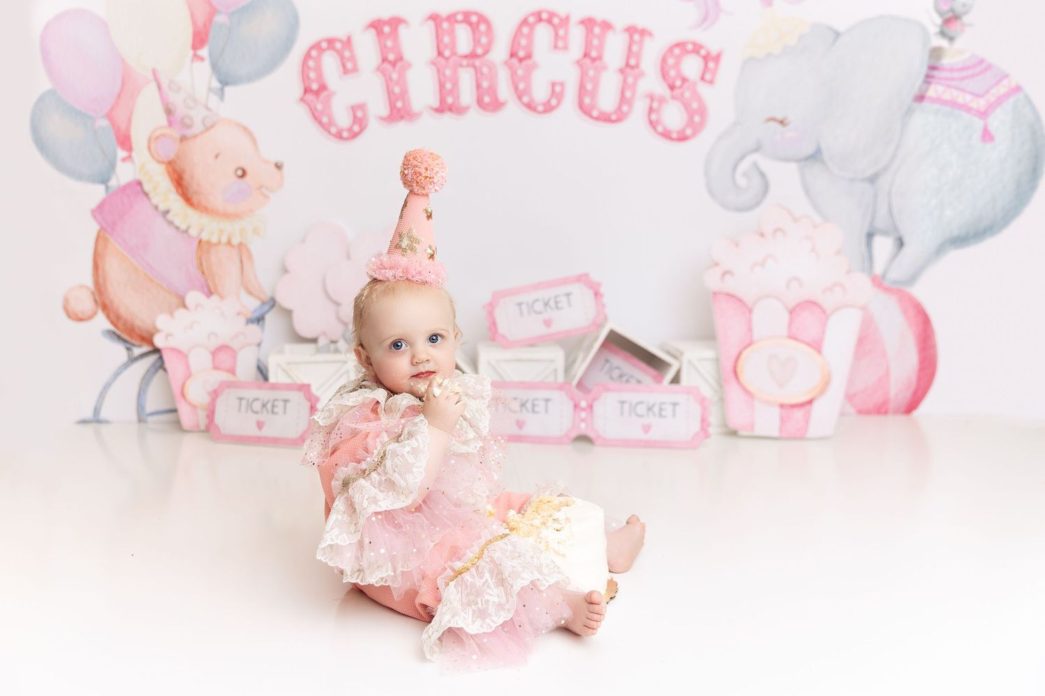 Circus-themed studio portrait with pastel decorations and baby in pink outfit.
