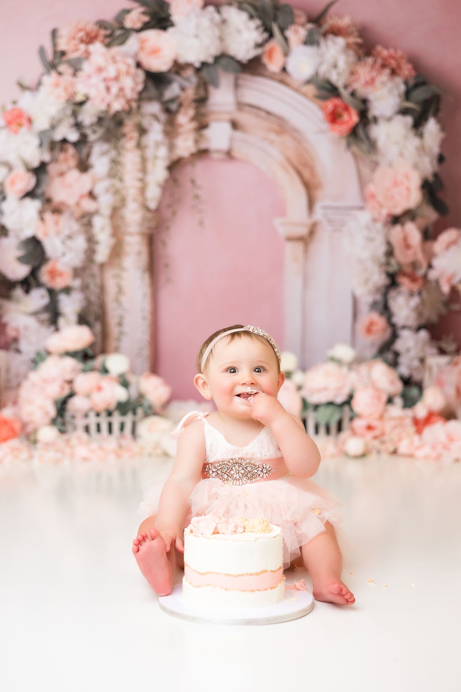 Pink floral cake smash photography setup with elegant decor and white floor.