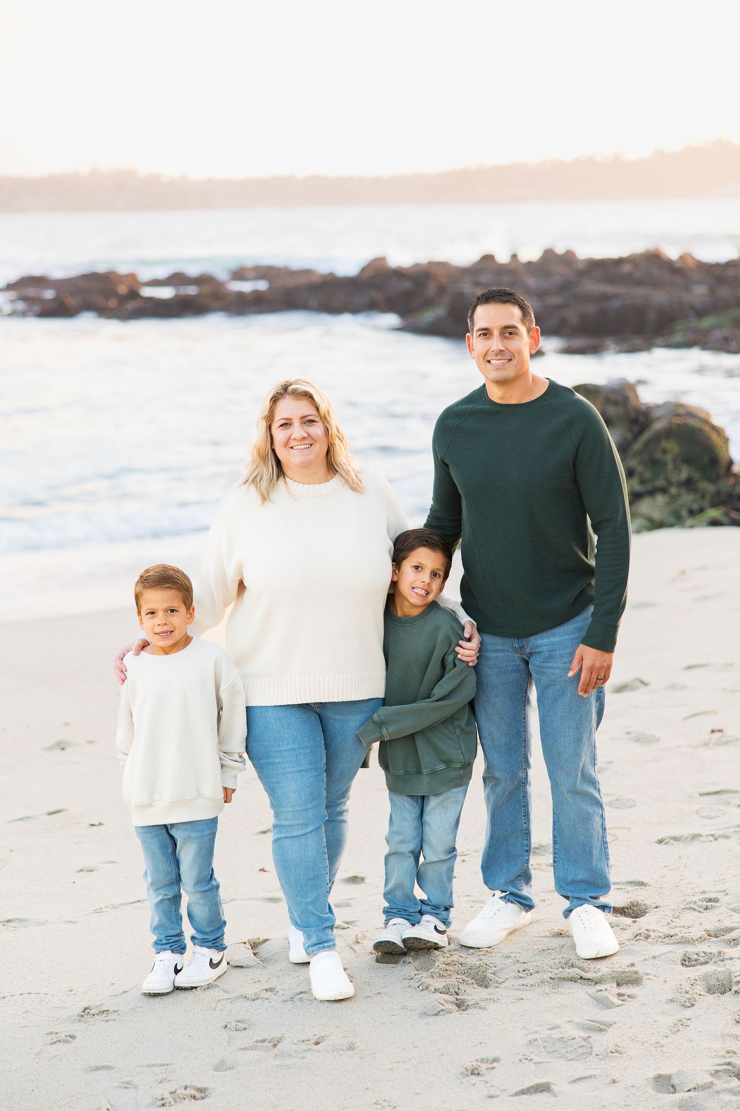 Family portrait on beach with matching casual outfits against ocean backdrop.