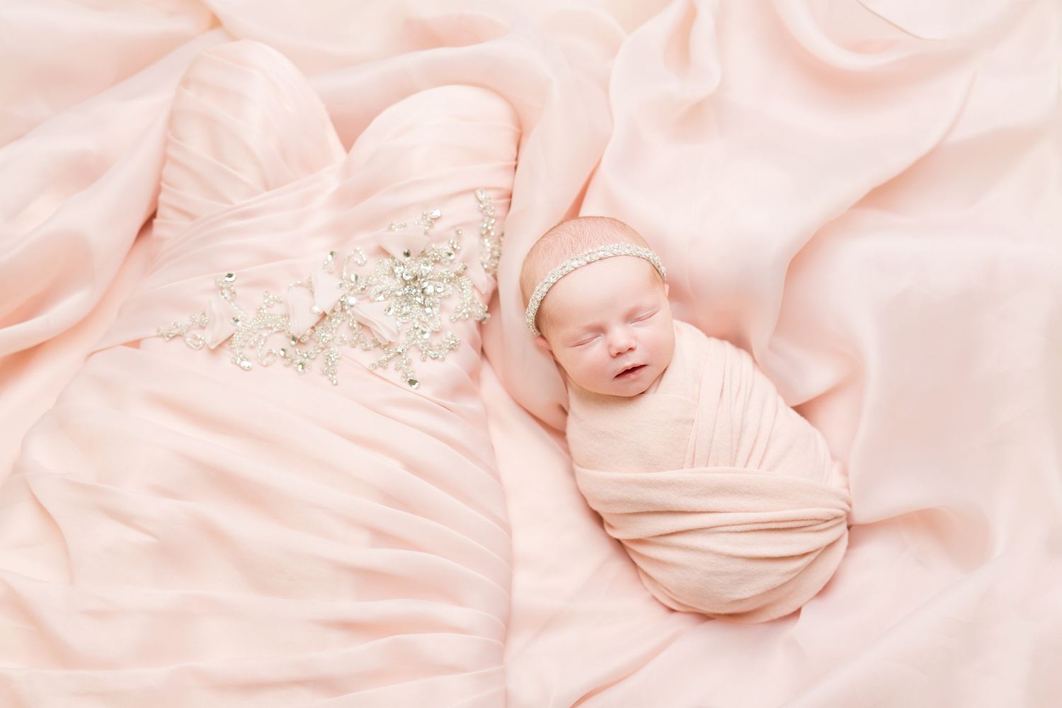 A collage of soft pink baby photos featuring a sleeping newborn wrapped in delicate fabric and lace textures.