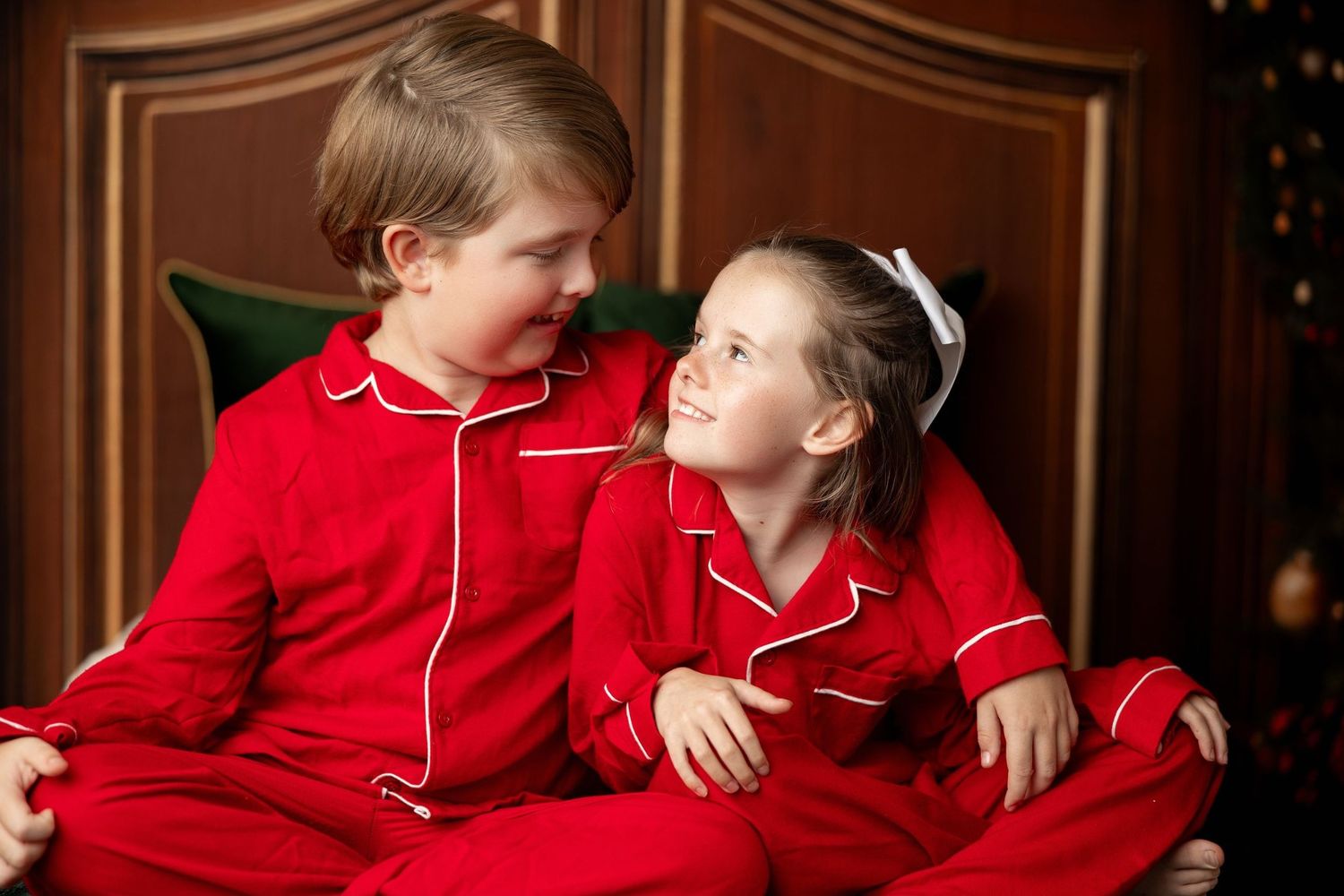 Two kids in matching red Christmas jammies smiling at a Milk & Cookies holiday mini session in Pacific Grove