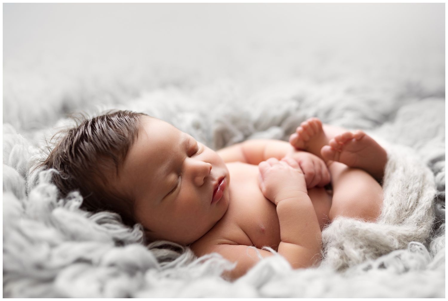 A peaceful sleeping newborn baby lies on soft gray blankets in a gentle natural light setting.