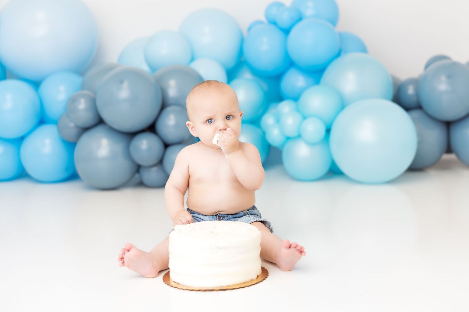 Adorable cake smash setup with blue balloon garland and white backdrop for special occasion photography.