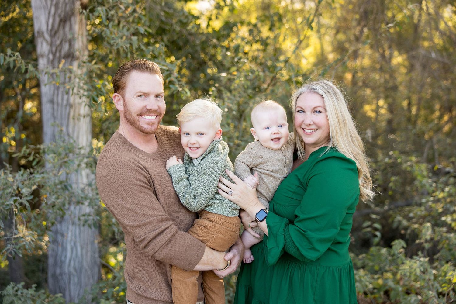 A loving family portrait session in an autumn forest with warm golden sunlight filtering through the trees.