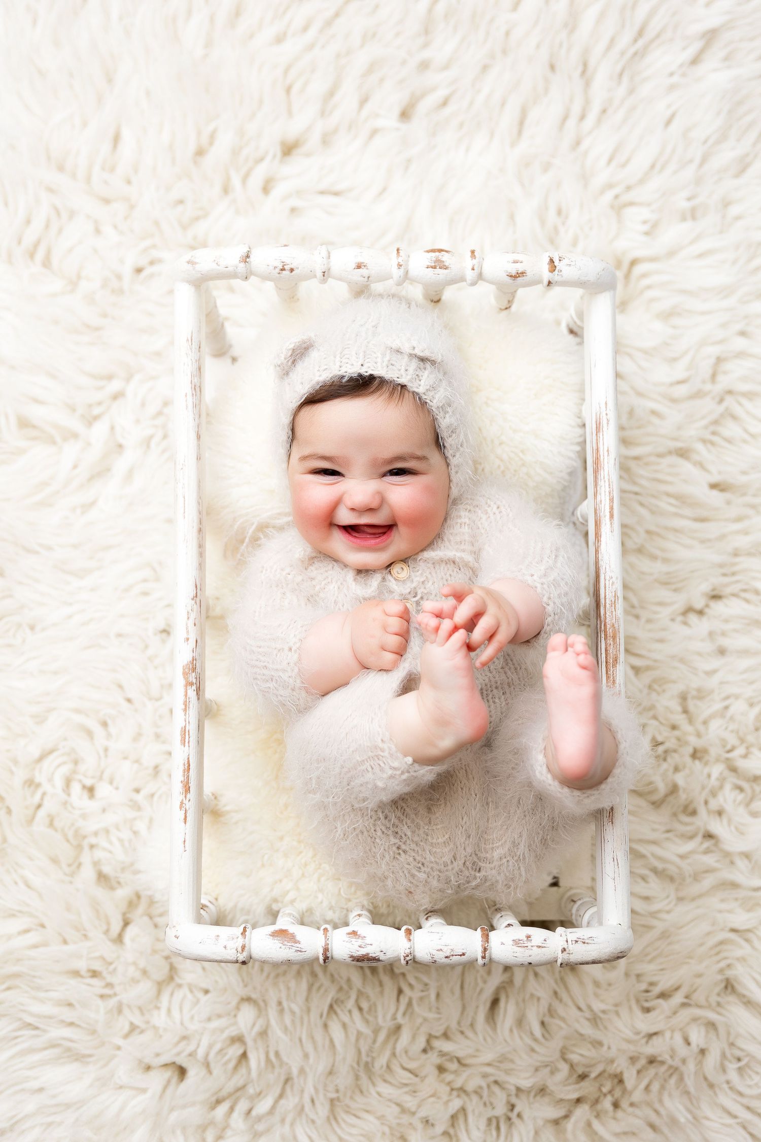 Joyful baby playing in vintage wooden crate on white fur rug.