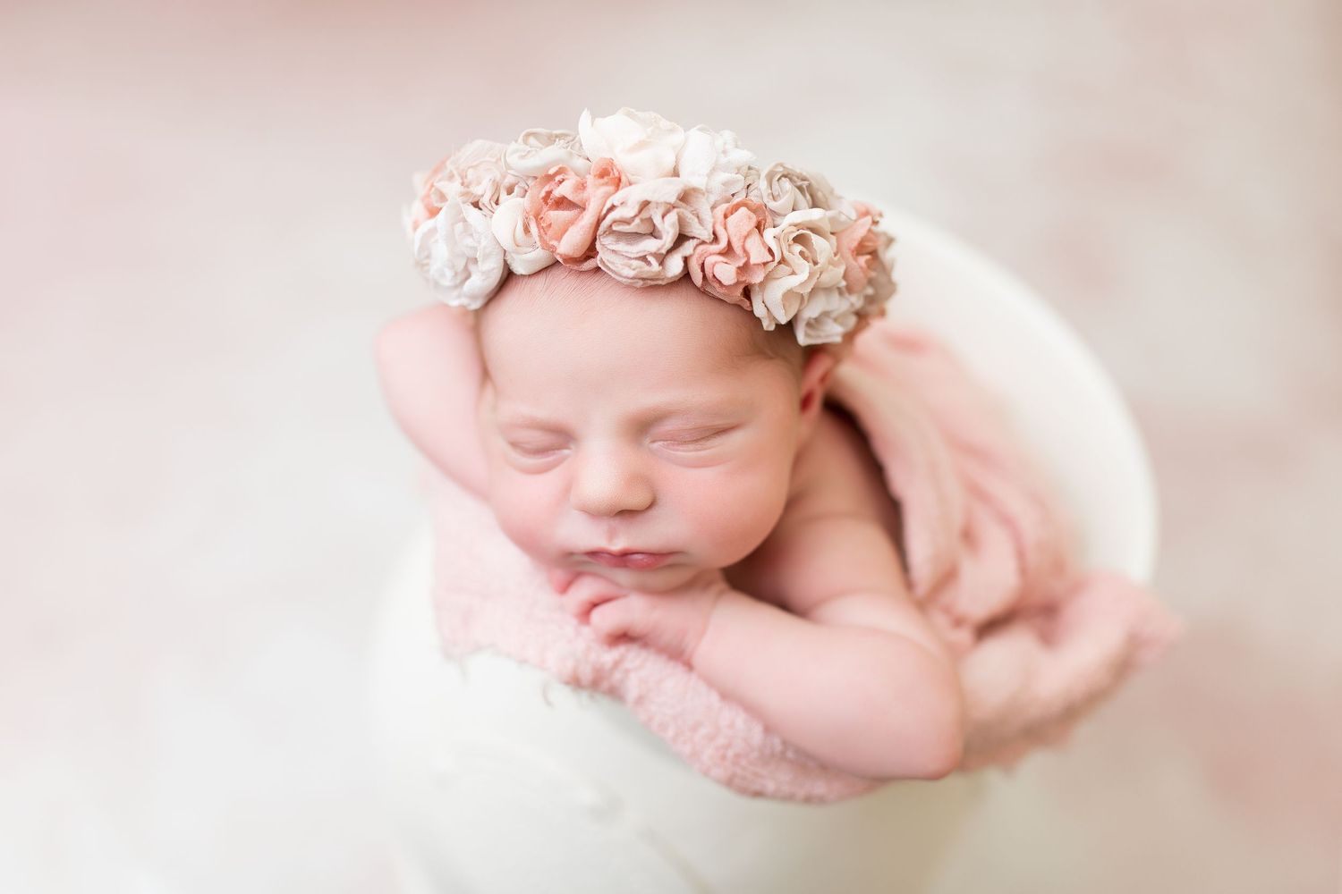 Sleeping newborn baby in pink wrap with delicate floral headband against soft background.
