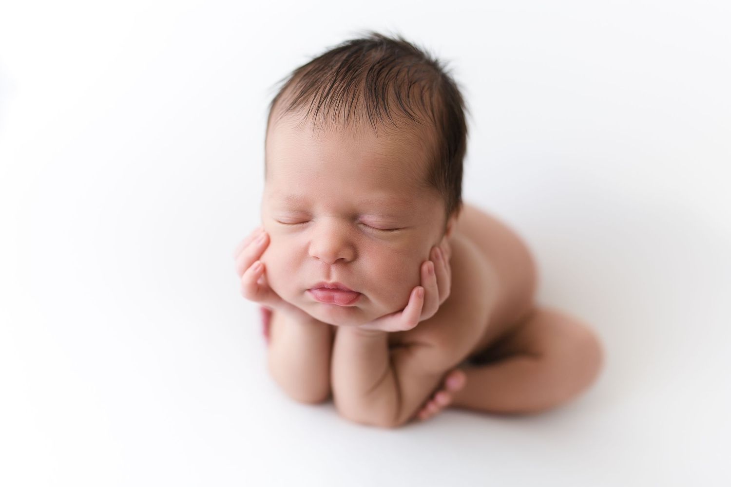 Sleeping newborn in frog pose on white background in gentle natural lighting.