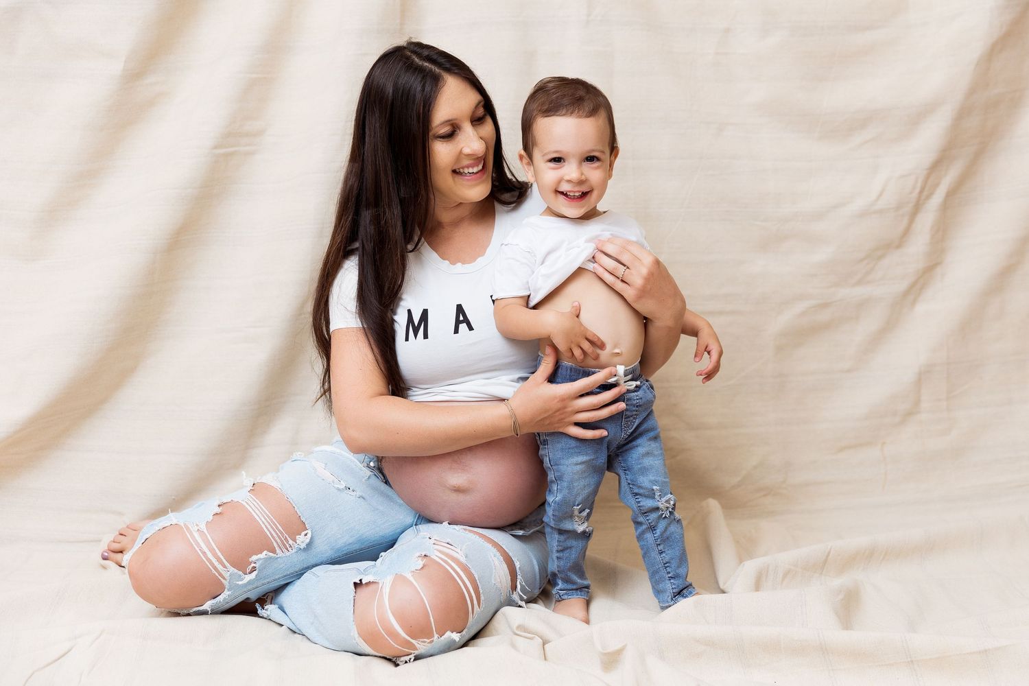 Maternity photo session with casual outfits against neutral beige backdrop.