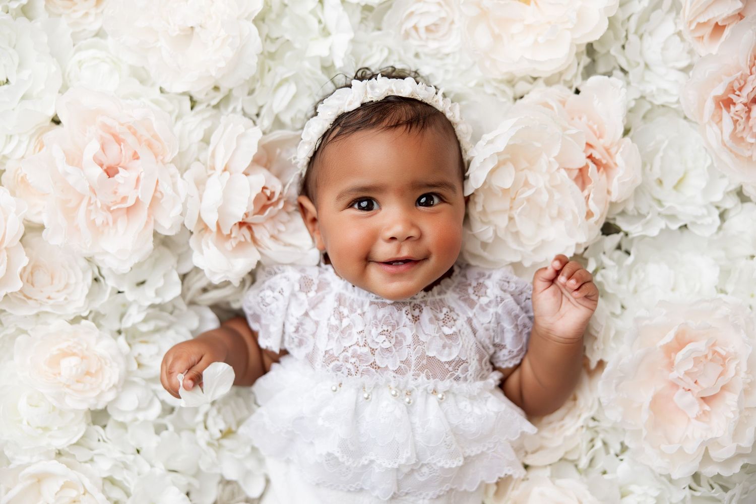 Four baby portraits against a floral backdrop with white and peach roses creating a soft, romantic setting.